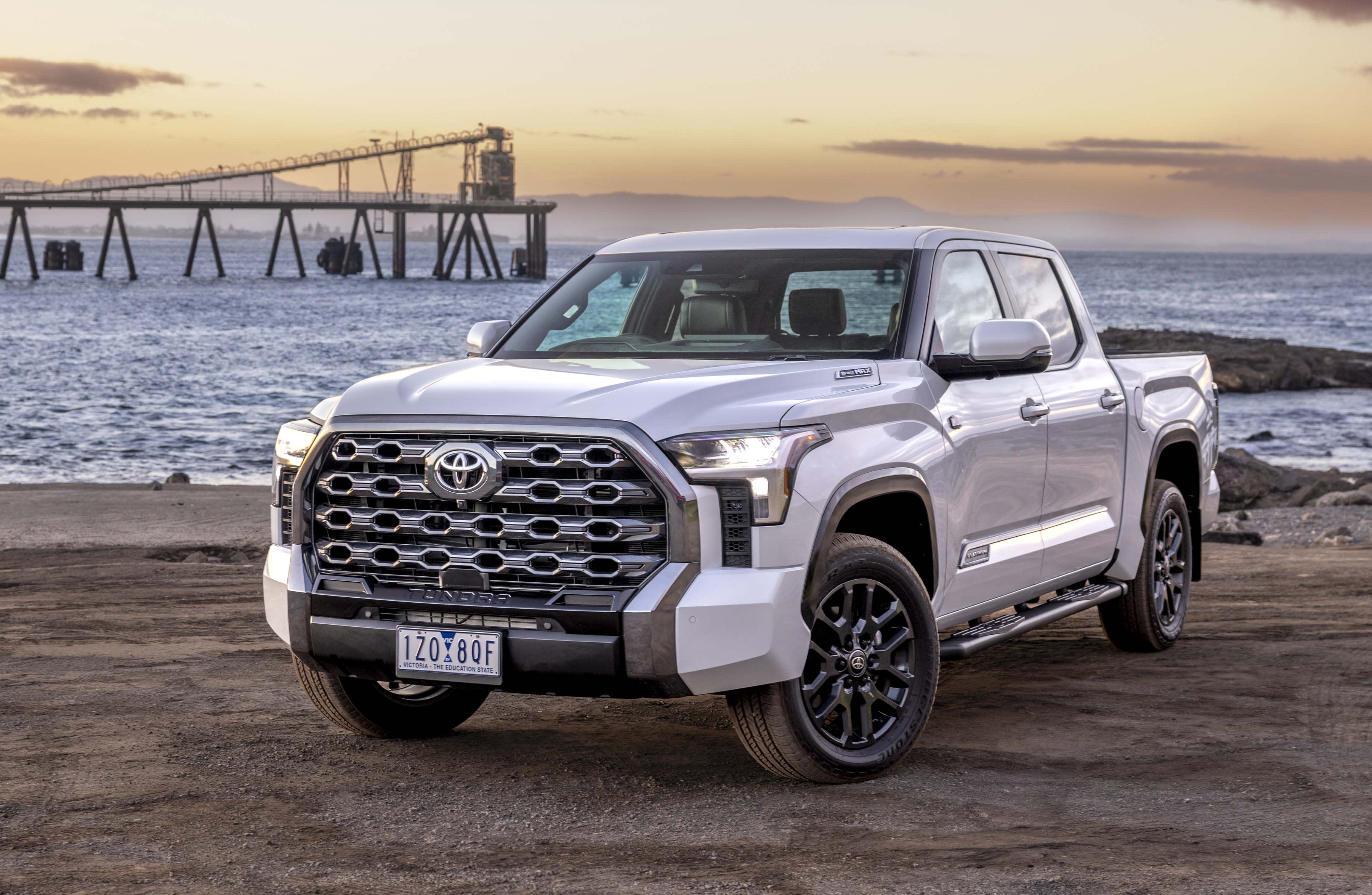 A white Toyota TUNDRA parked on sand near a harbour
