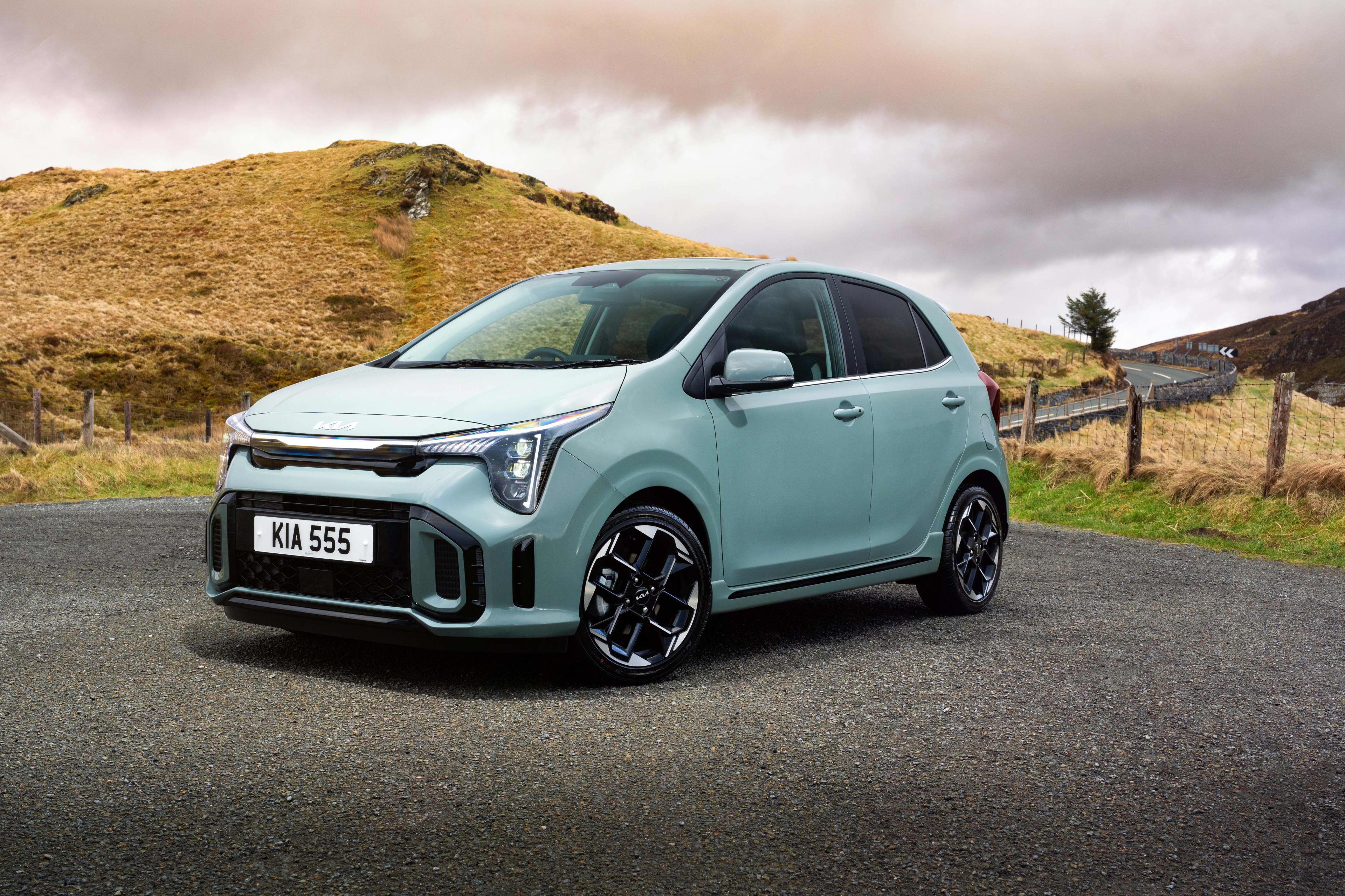 A light green Kia Picanto parked near a hill in a regional setting