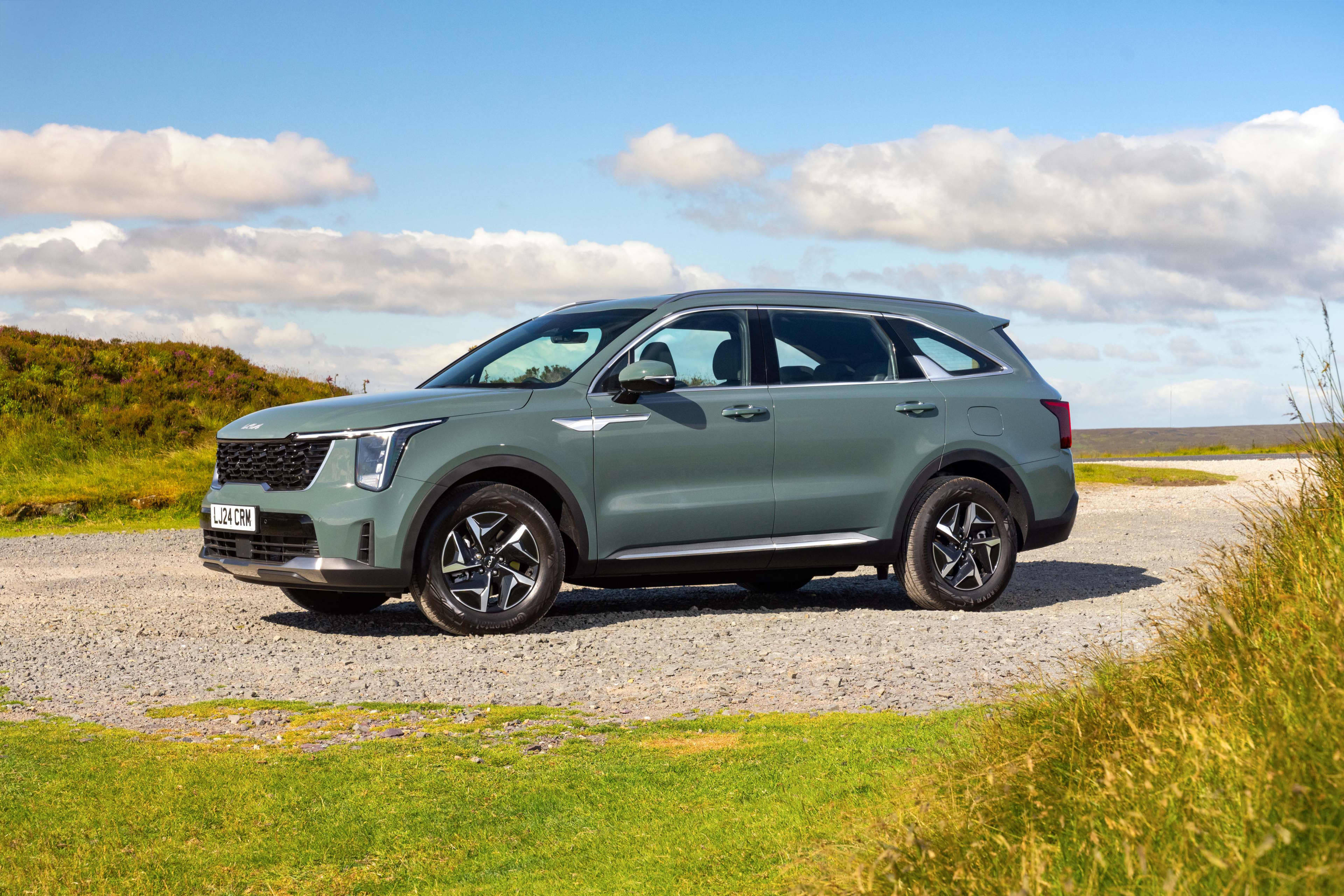 A green Kia Sorrento parked on a gravel surface in a country setting
