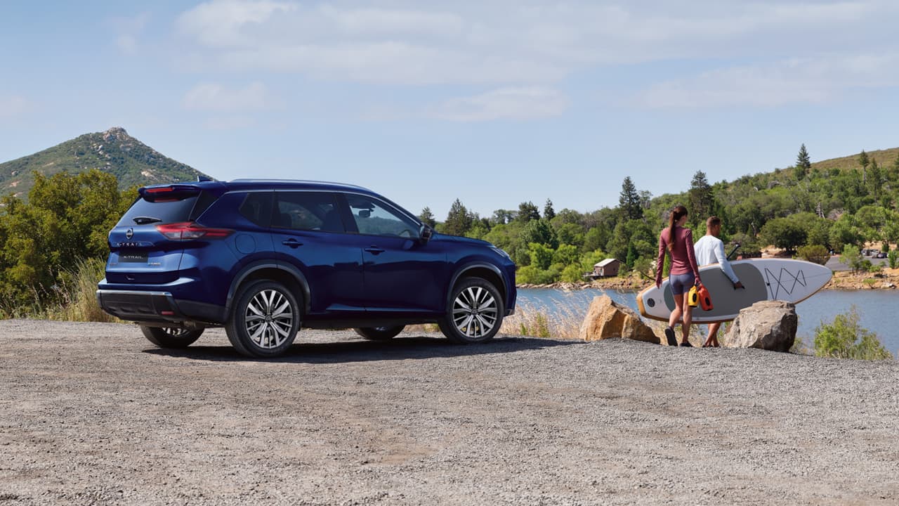 A dark blue Nissan X-Trail parked near a lake