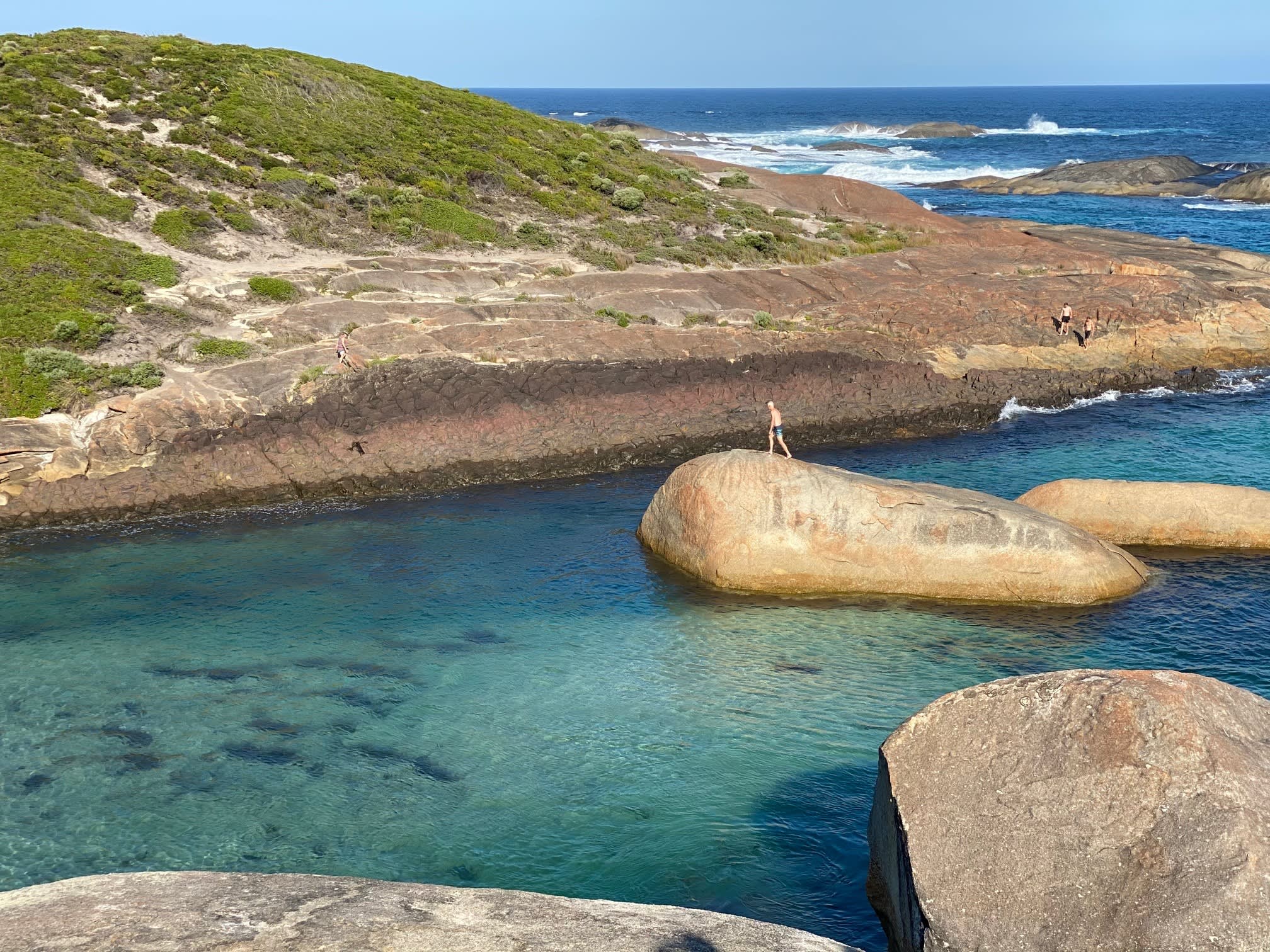 Rocks surrounded by turquoise water and granite landscape with bushland.