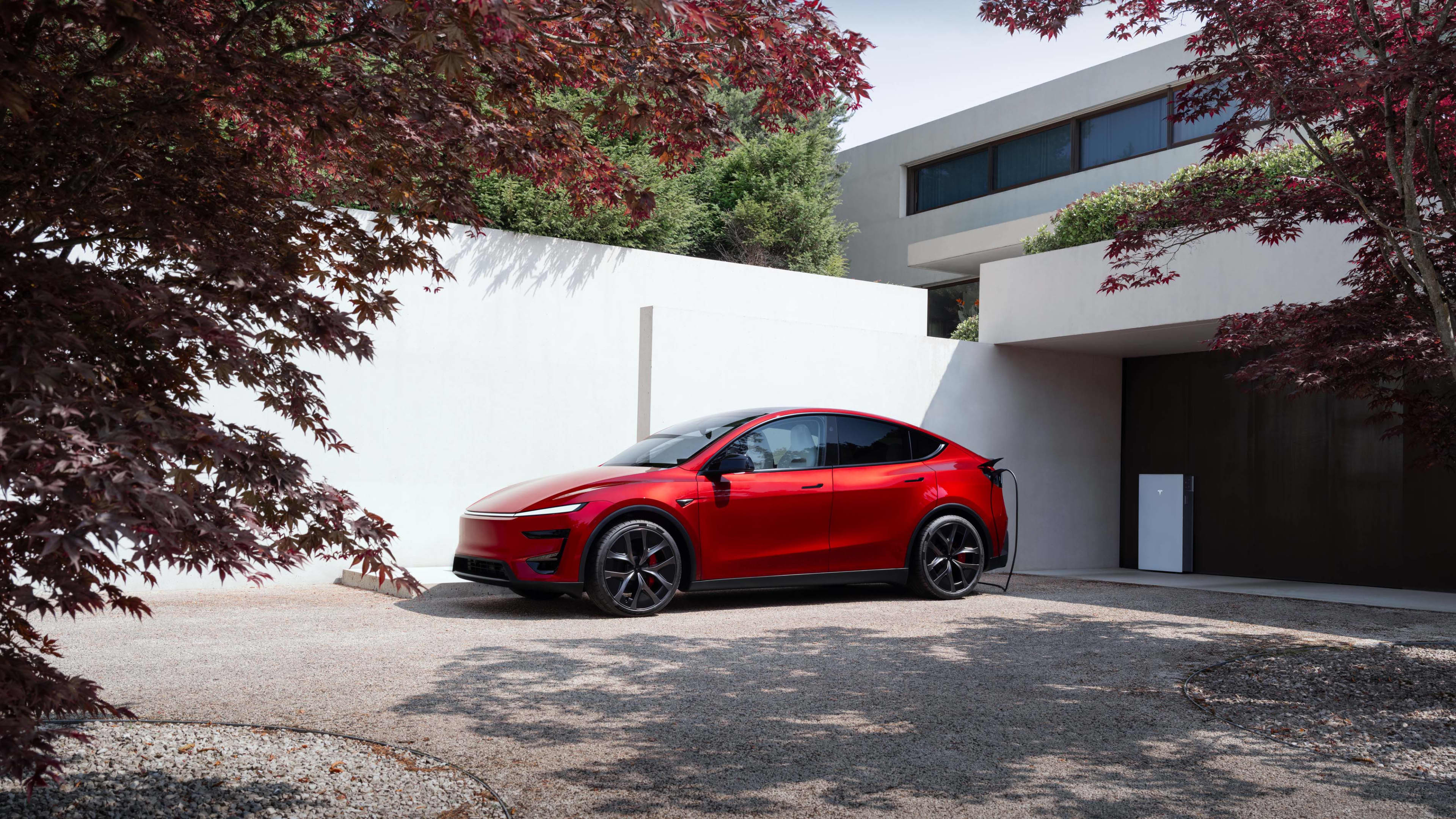 A red Tesla Model Y parked outside a modern home