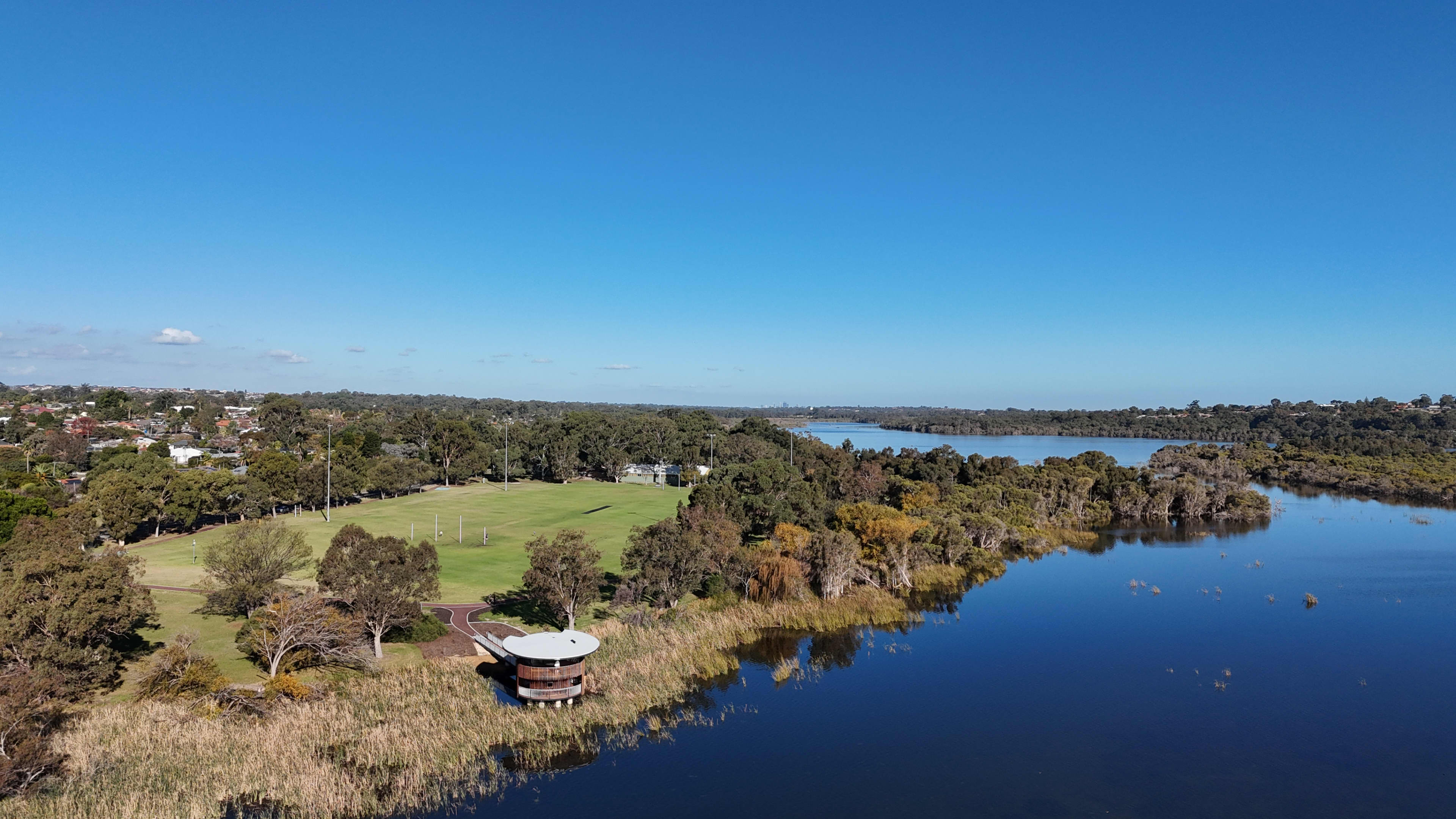 Aerial view of large freshwater lake with reeds, an oval and a two-level viewing structure on the banks of the lake.