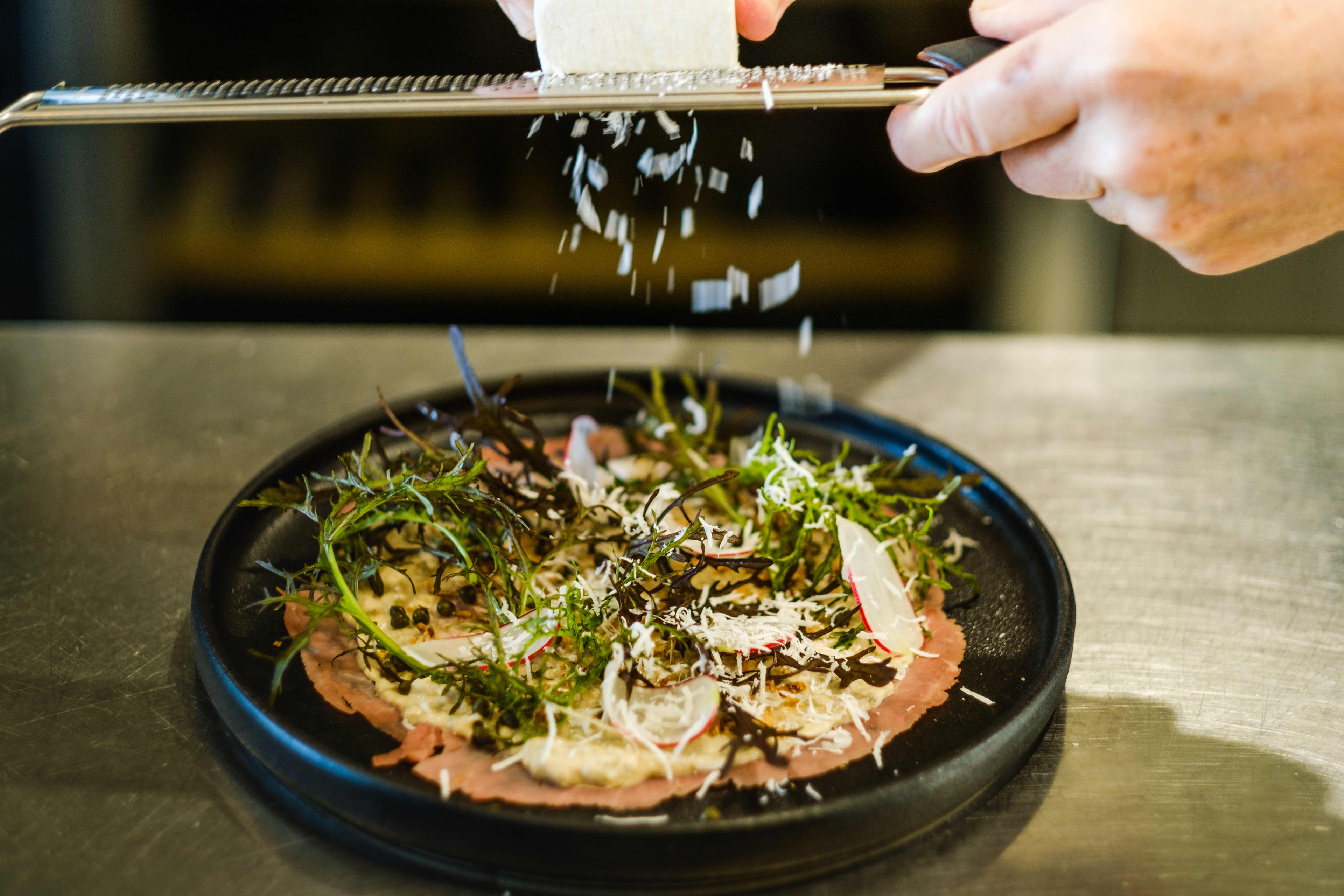 Cheese being grated above pizze-like dish.