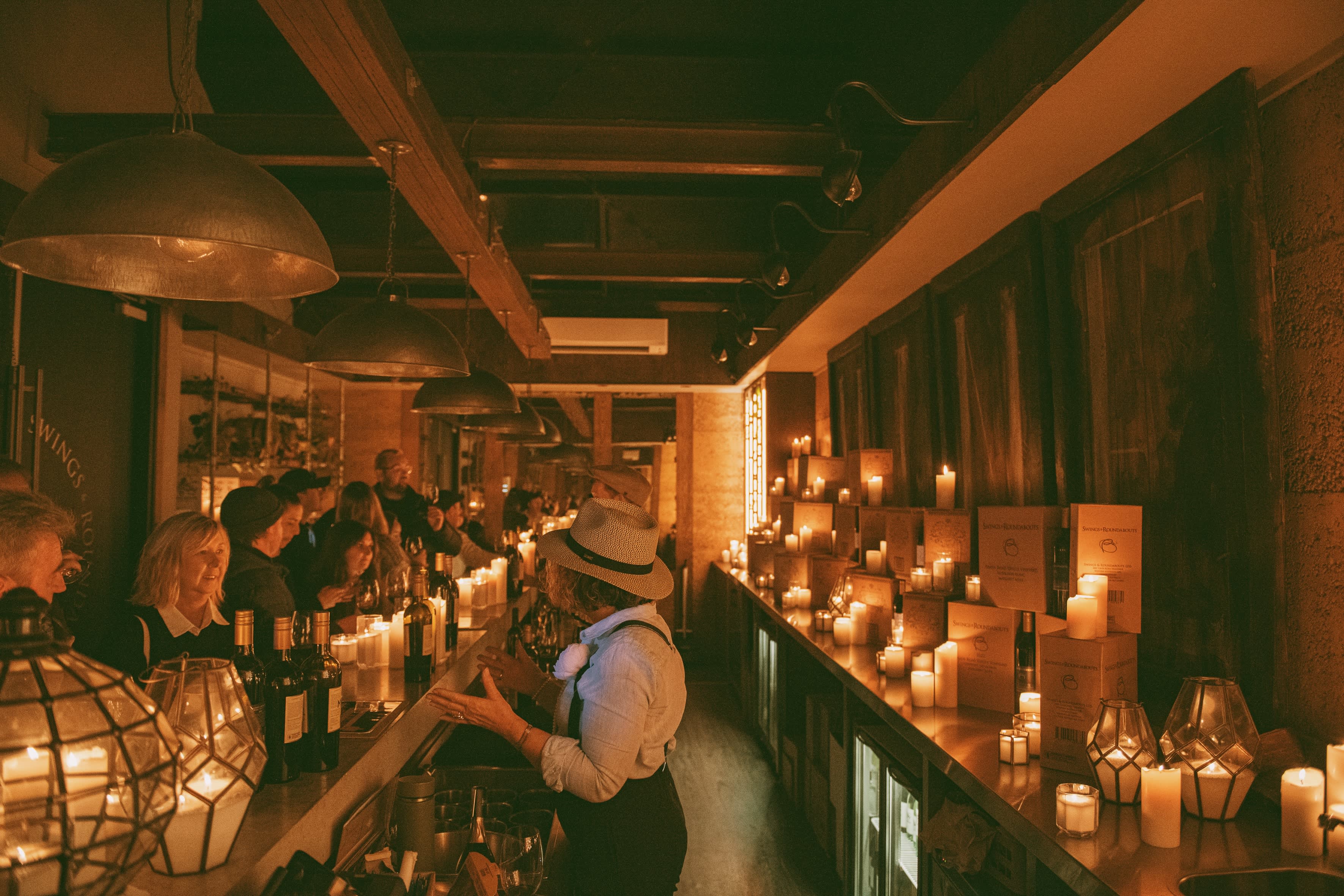Dark fireside setting indoors with candles and people working behind a bar in moody room.