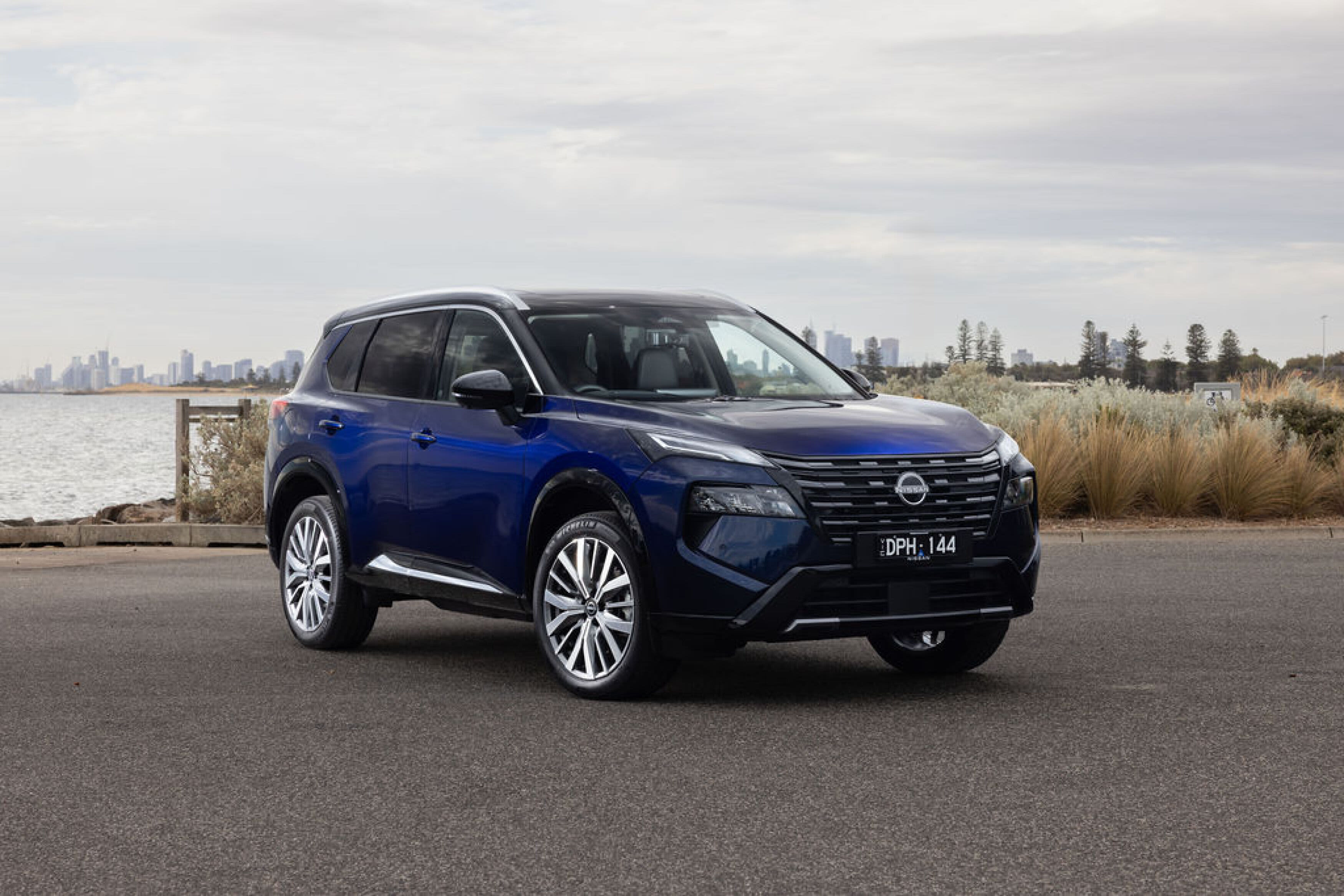 A blue 7-seat Nissan X-Trail parked near a beach