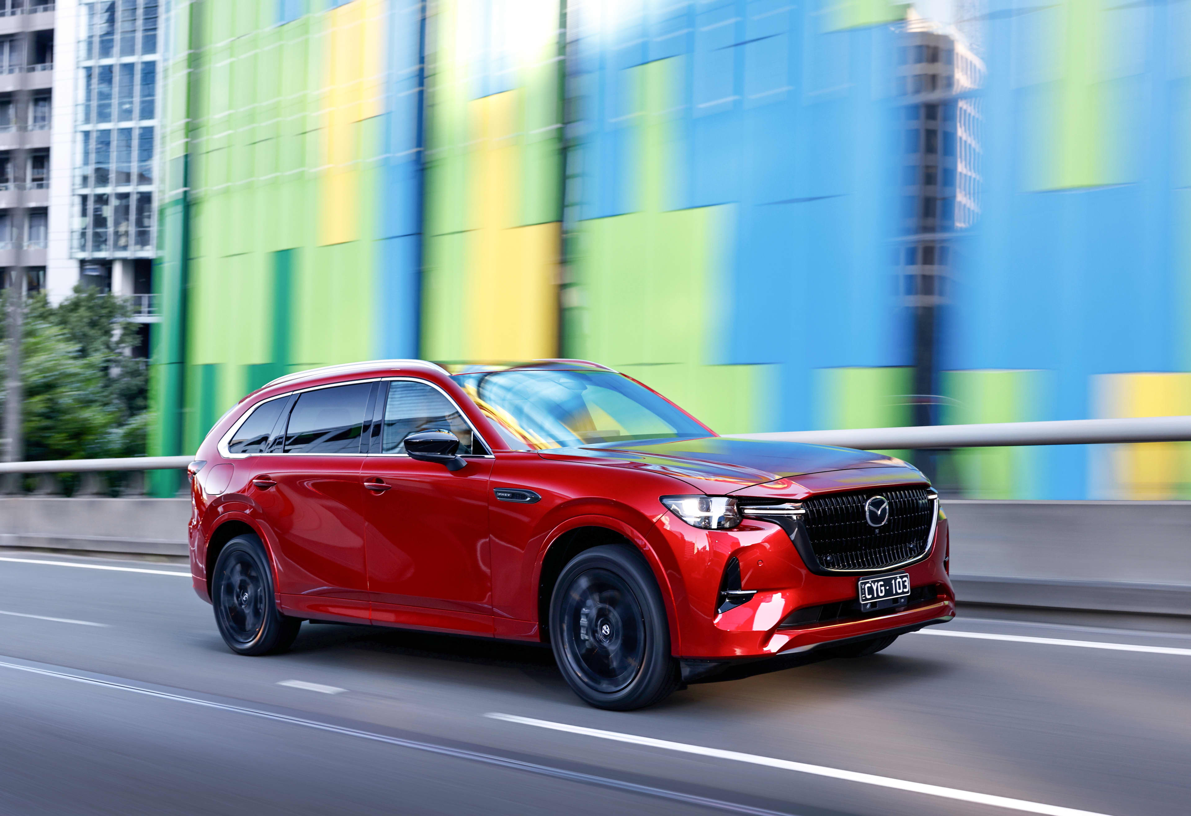 A red Mazda CX-80 driving on a city street