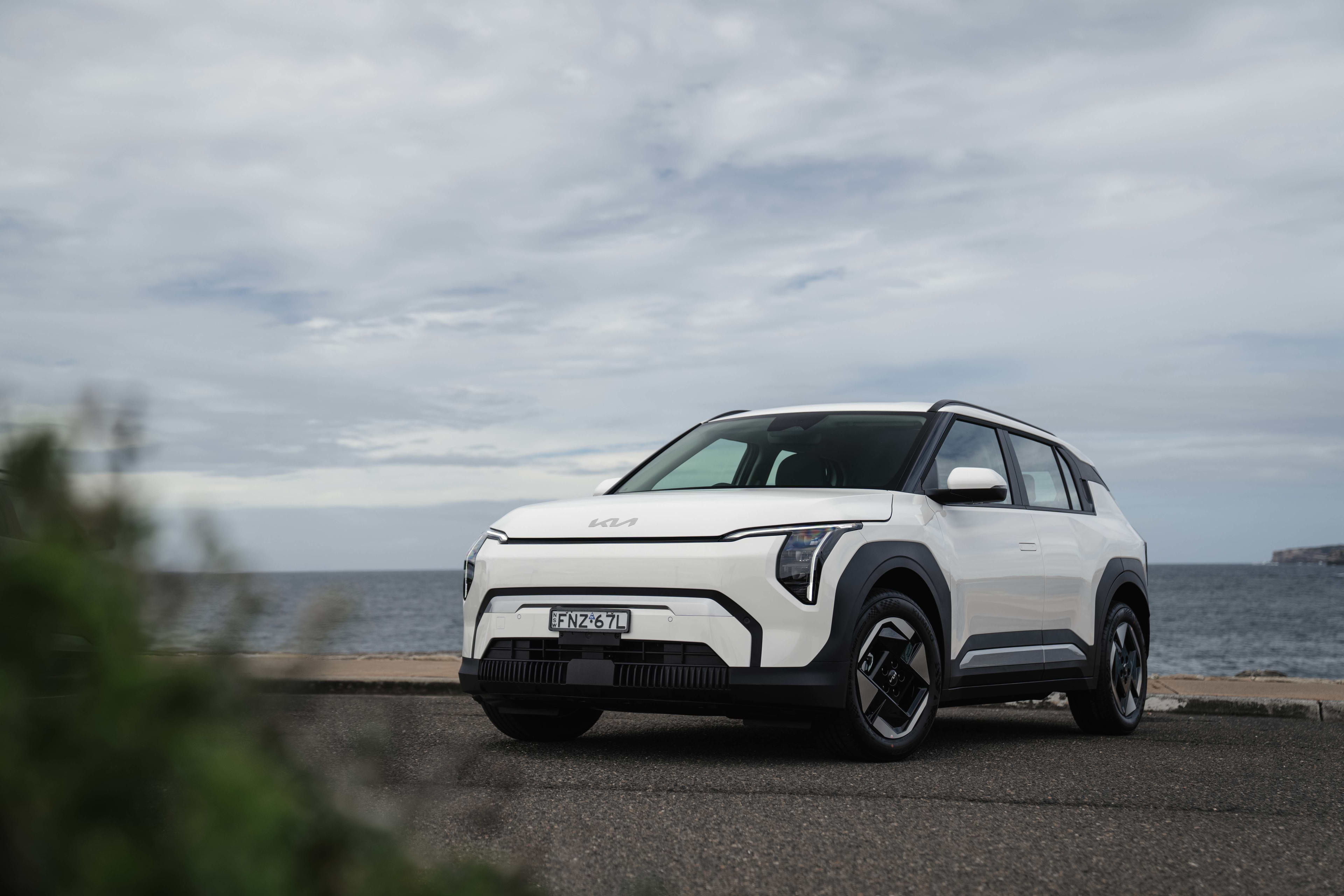 A white Kia EV 3 Air parked near a beach