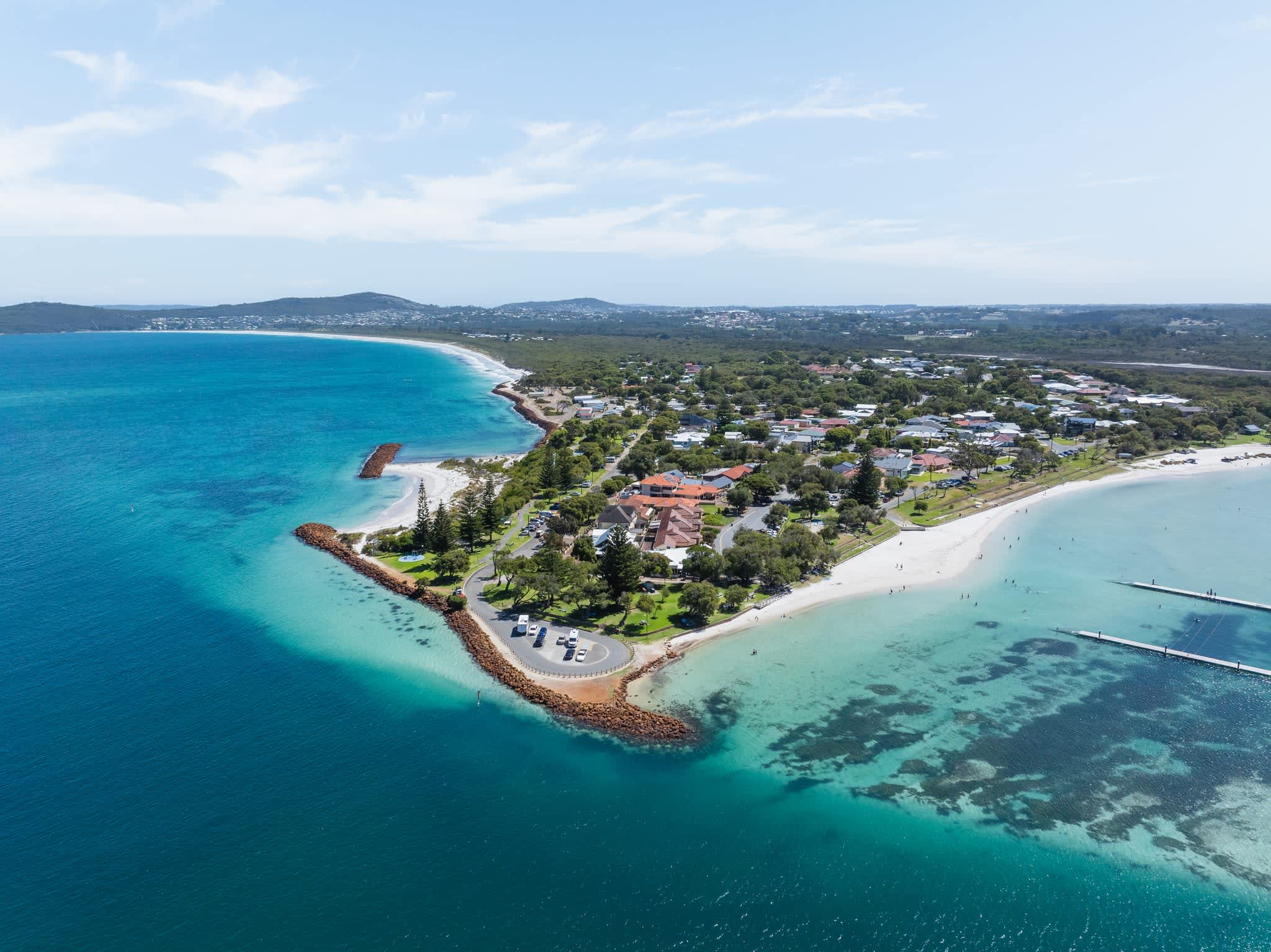 Aerial view of turquoise waters and land with car parking and buildings