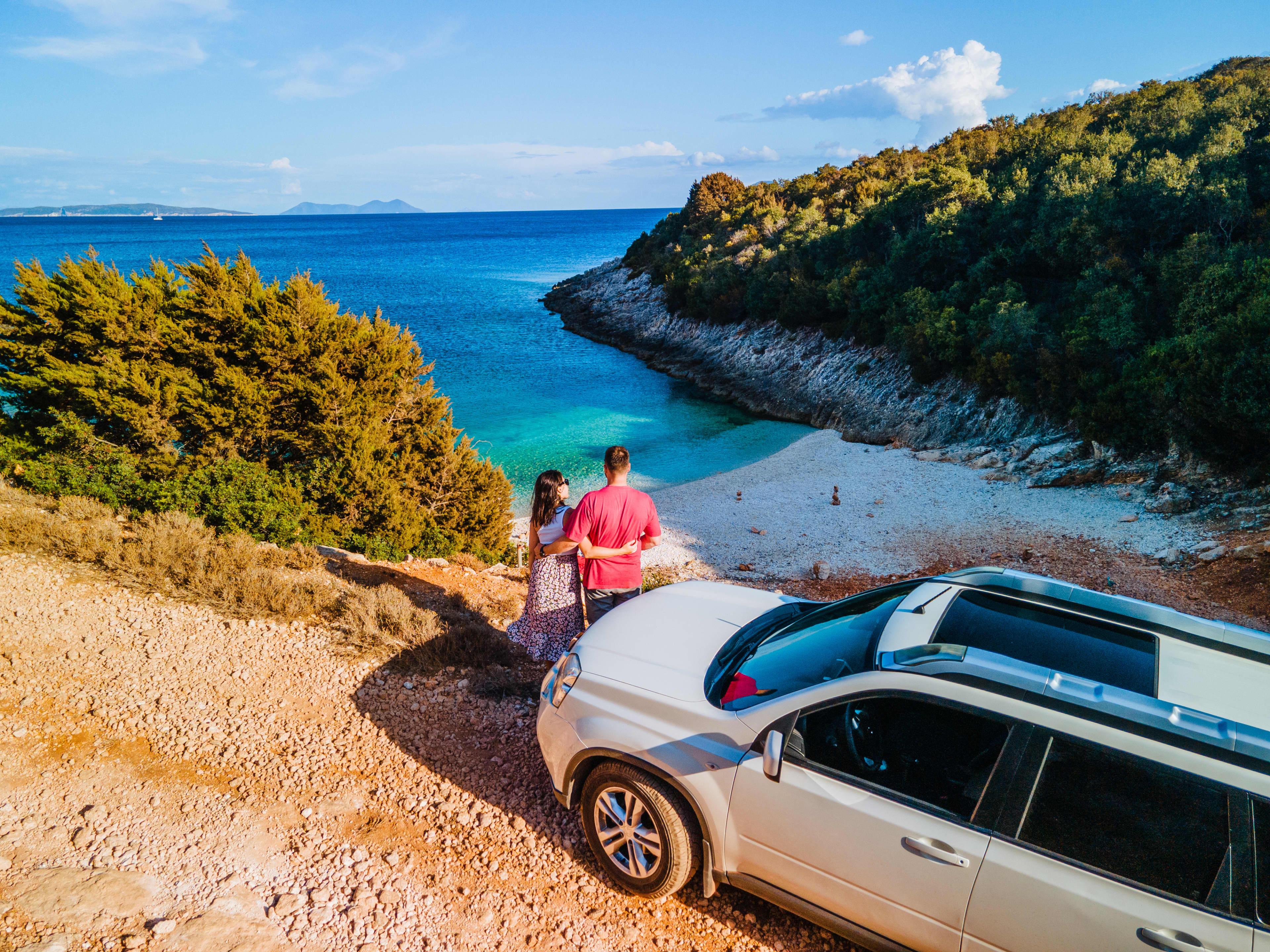 Couple standing in front of car overlooking turquoise beach on holidays