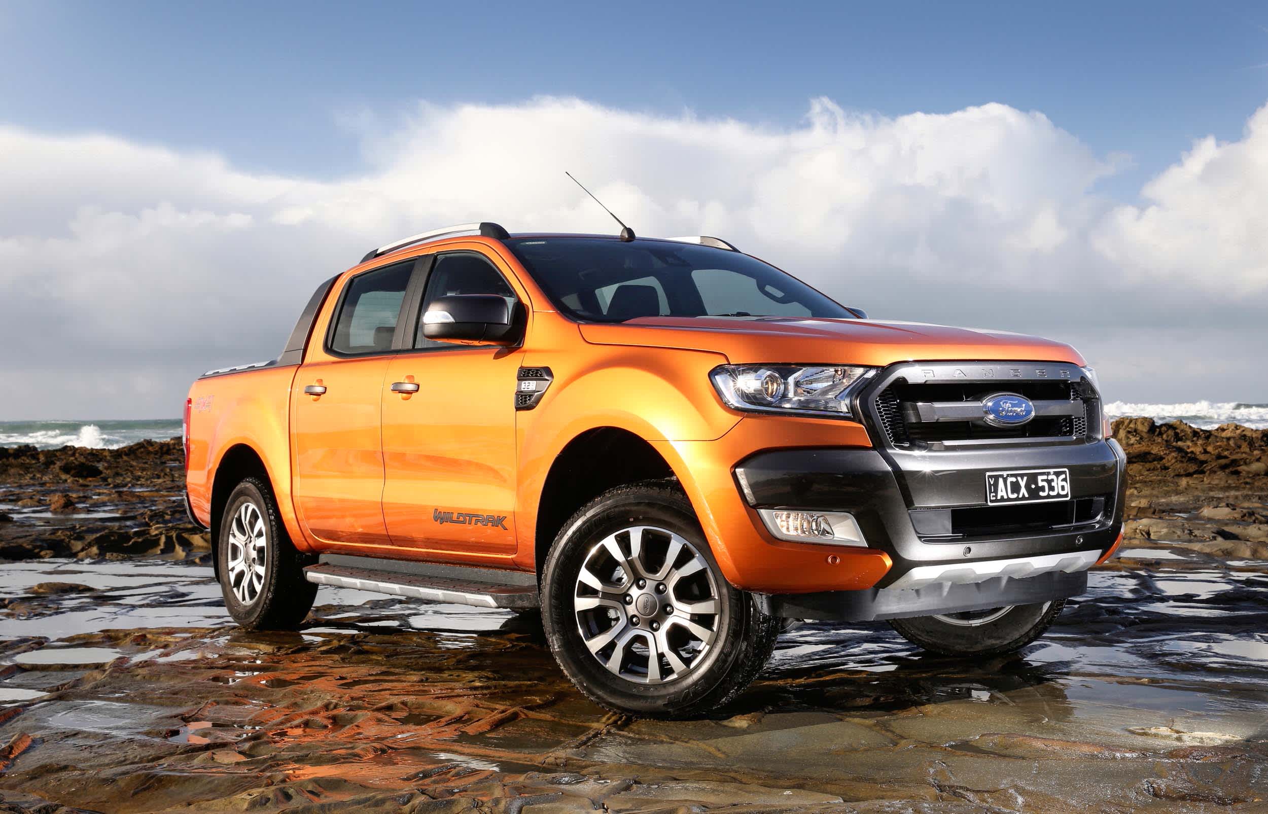A bronze Ford Ranger parked on rocks near a beach