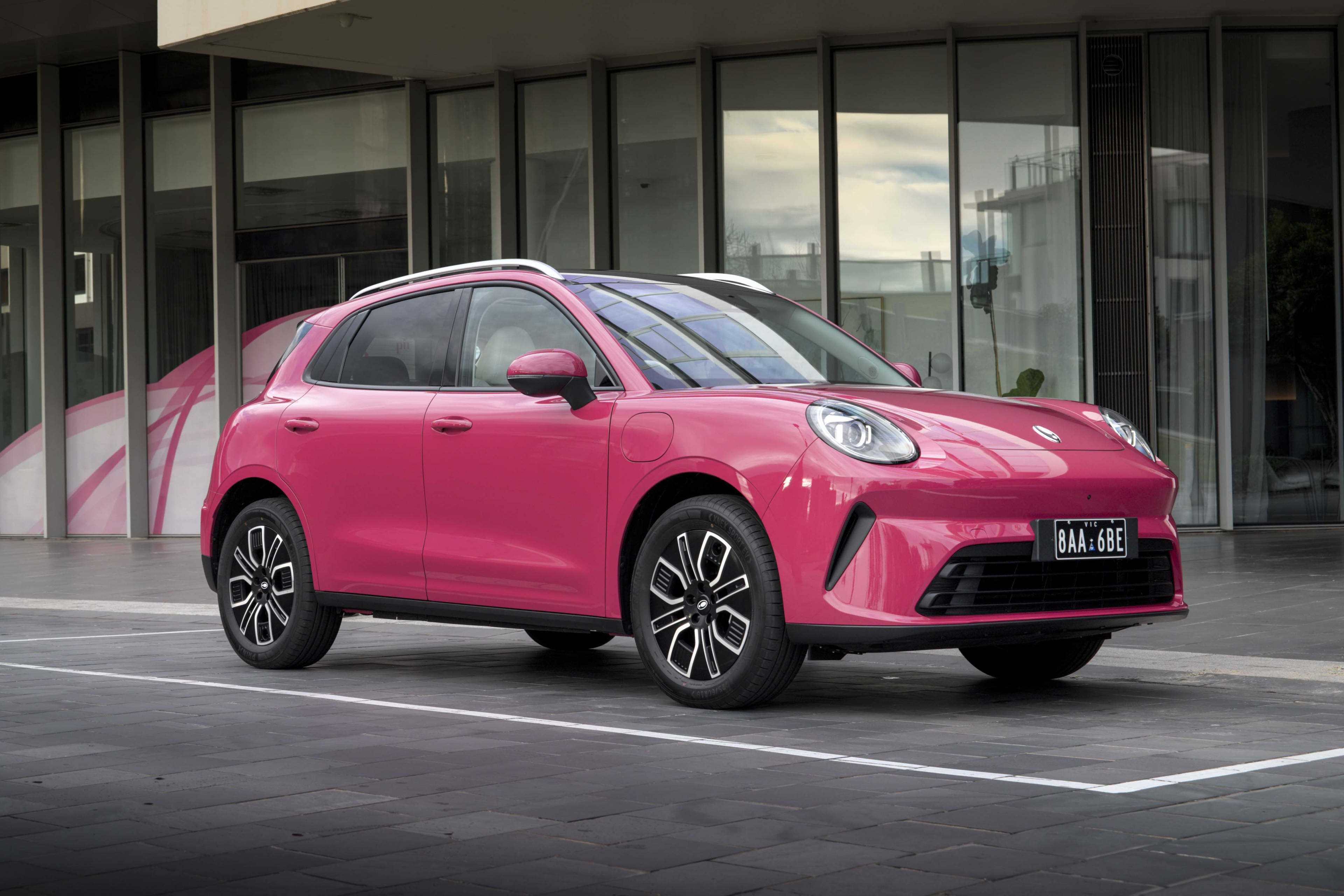 A pink GWM Ora 5 Lux parked near a city building