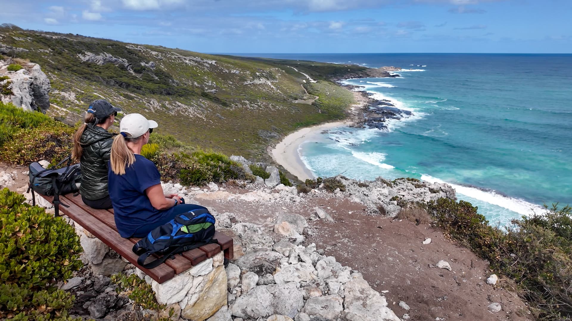 Two people sitting on a bench on walking trail overlooking ocean