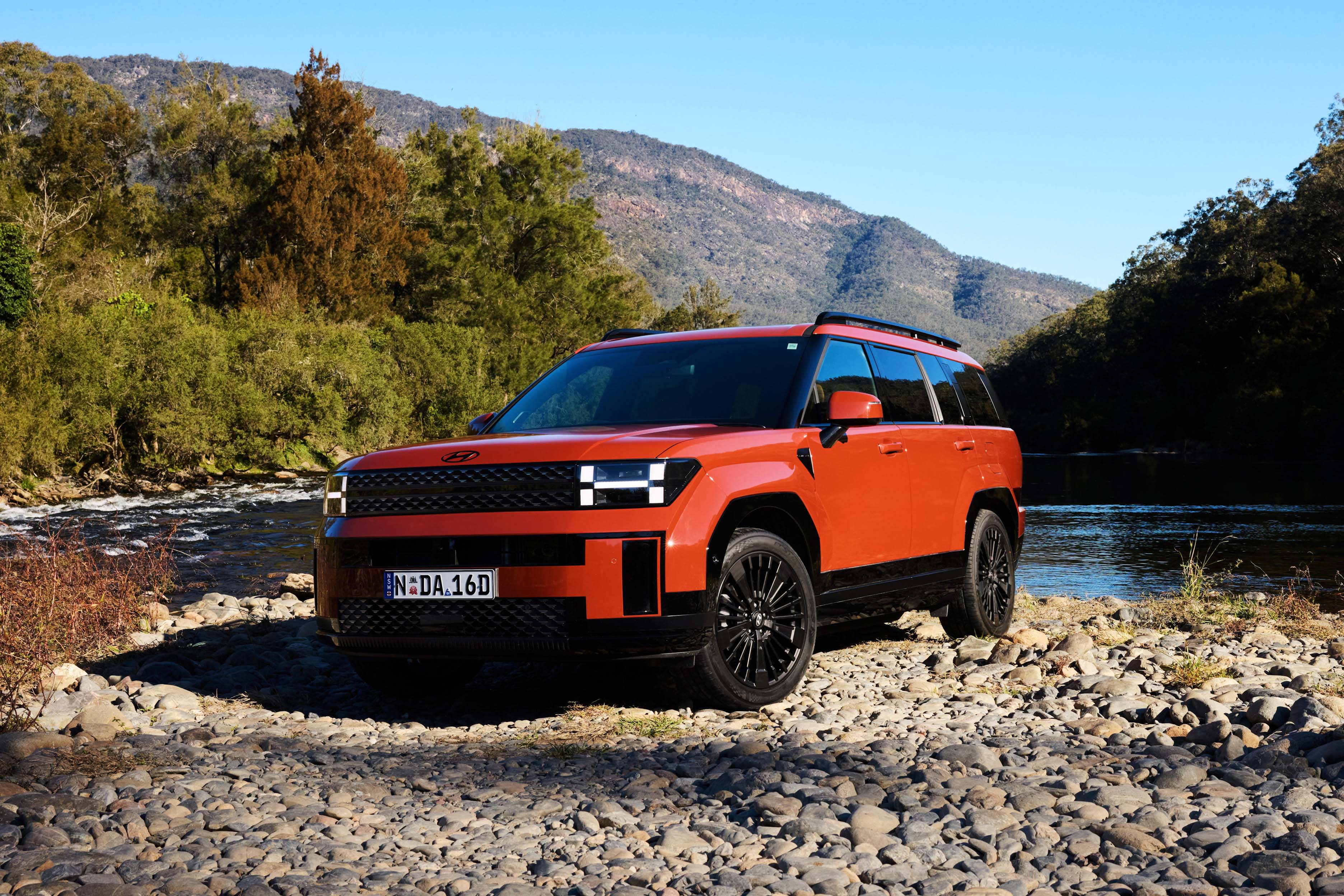 A red Hyundai SANTA FE parked on rocks near a creek
