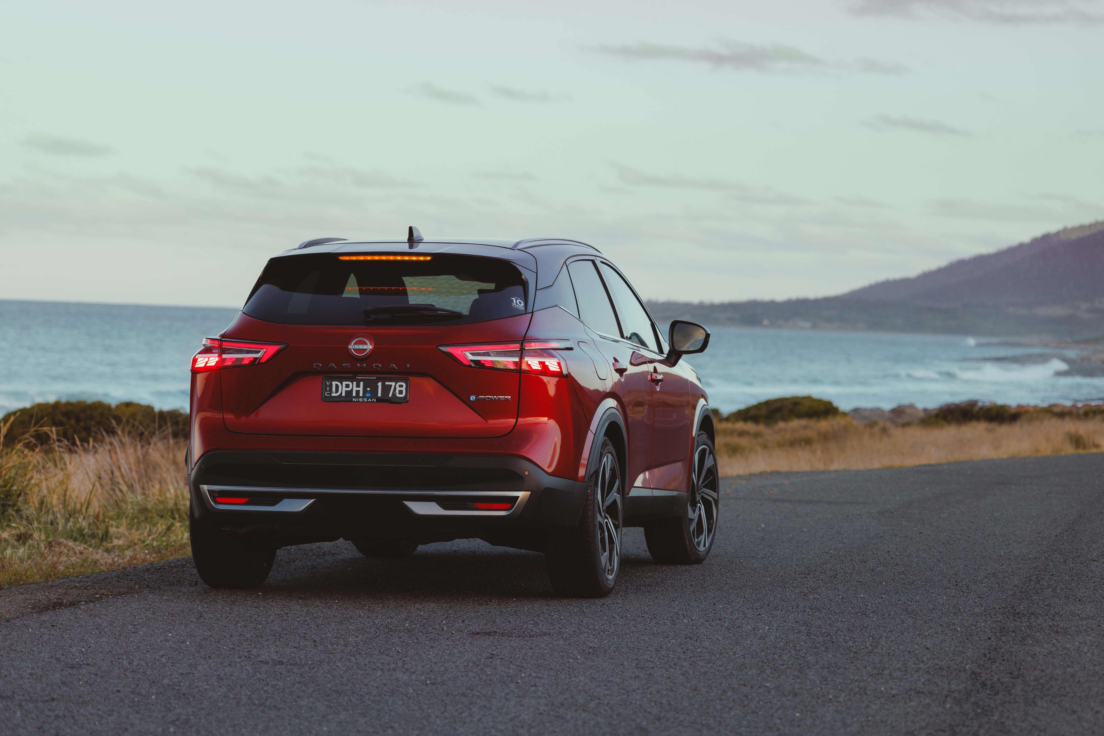 A red Nissan Qashqai e-power driving on a coastal road