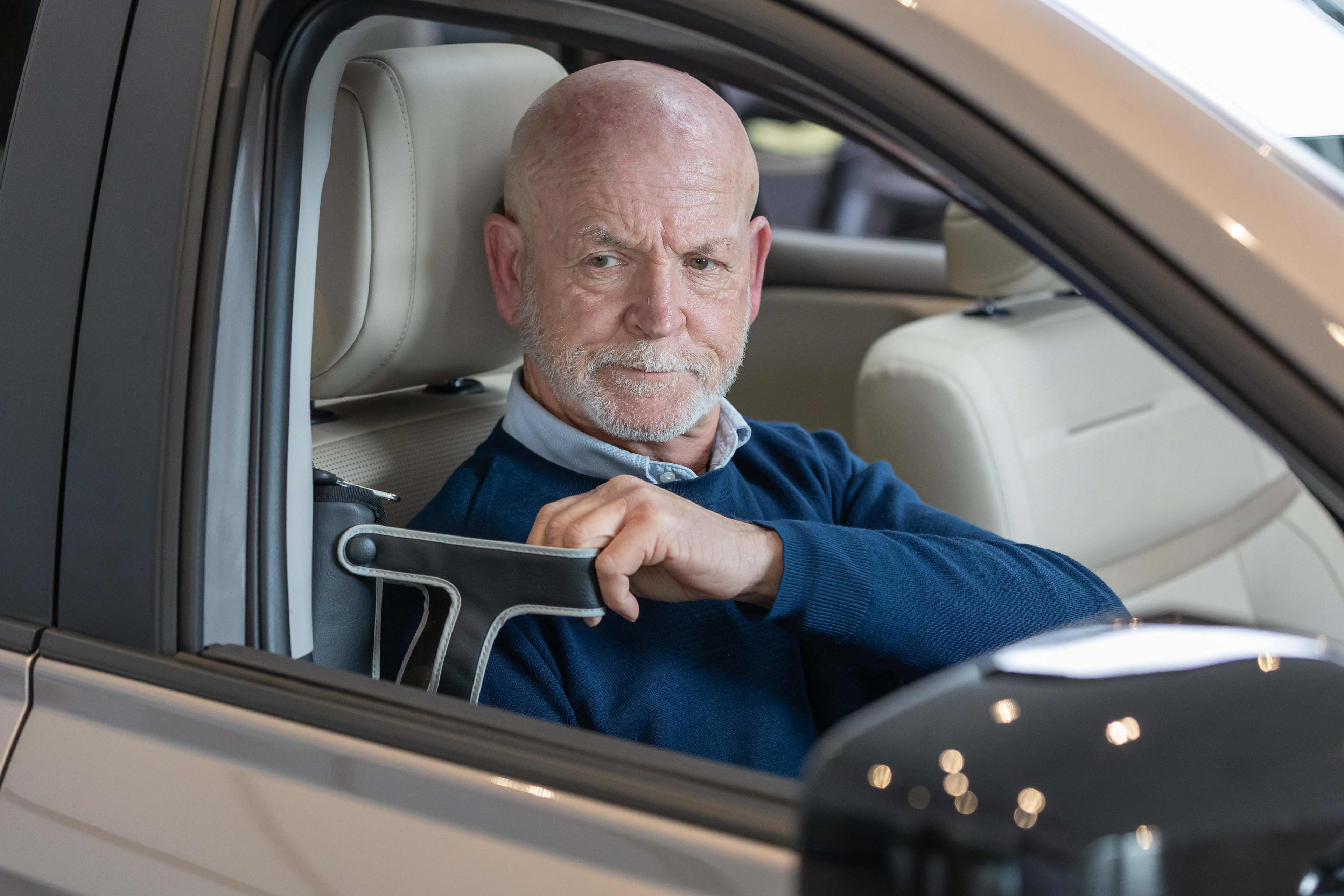 A man seated in a drivers seat of a car pulling on a seatbelt