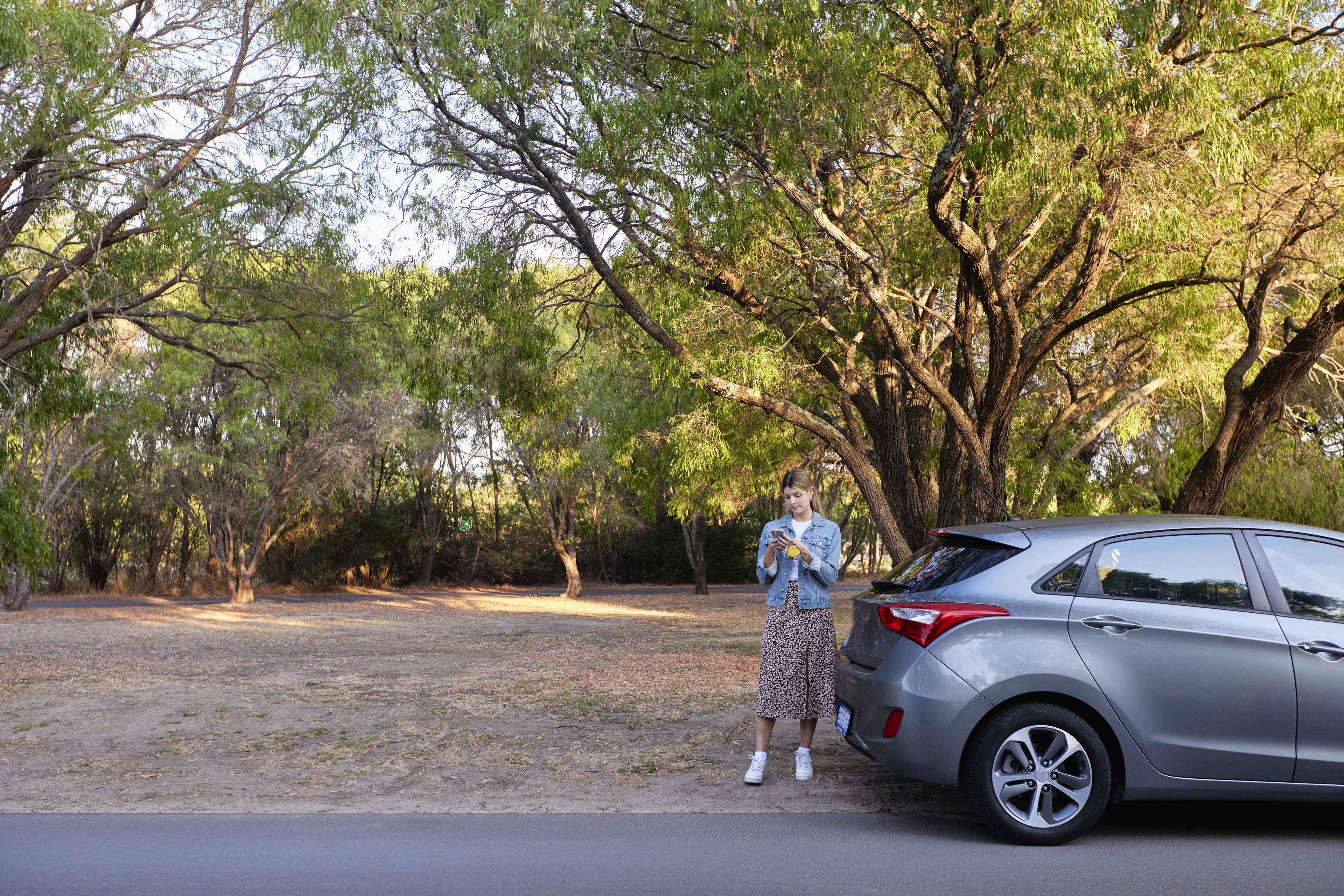 Woman using mobile phone outside parked car on side of road