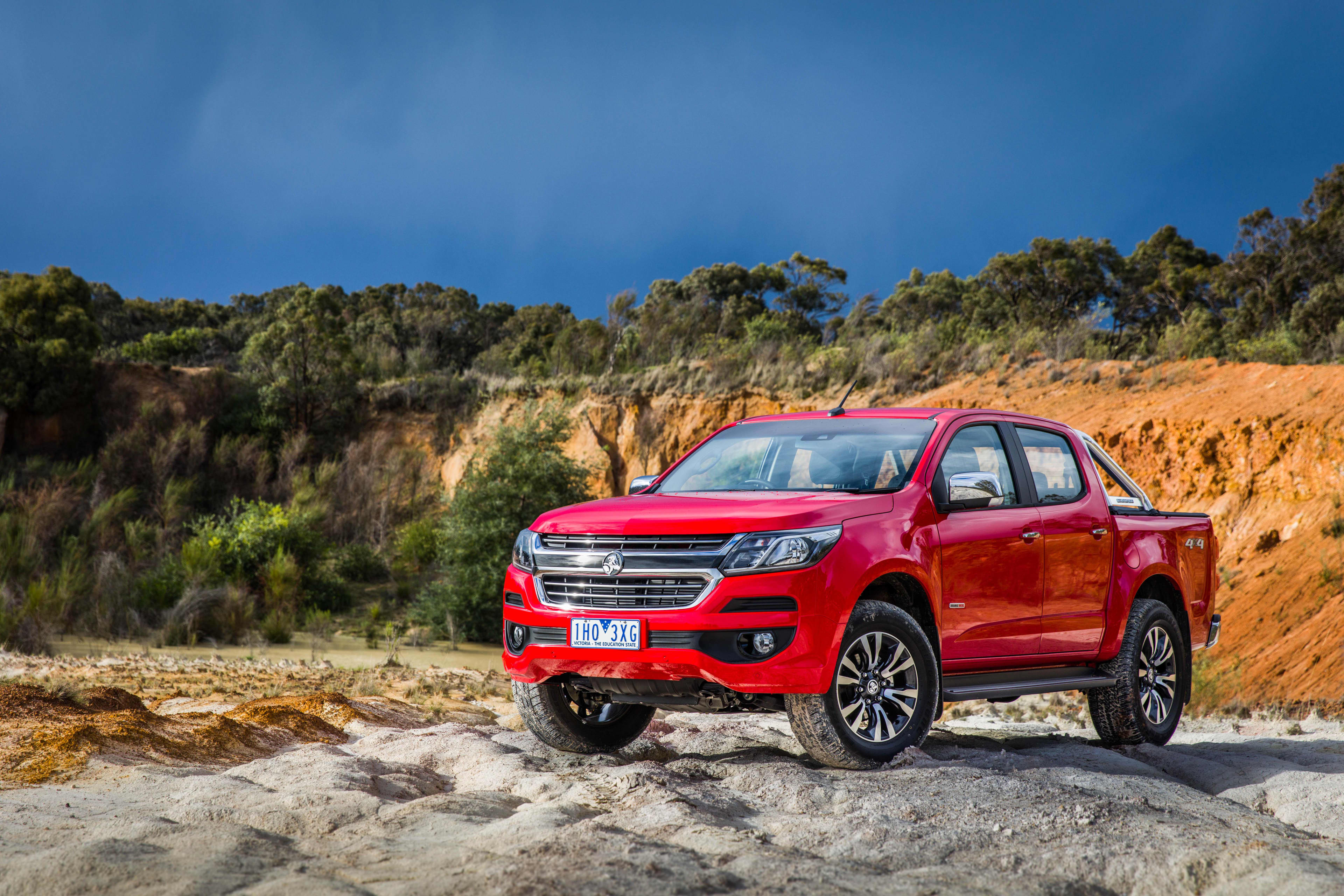 A red Holden Colorado parked on a rocky surface in a rural landscape