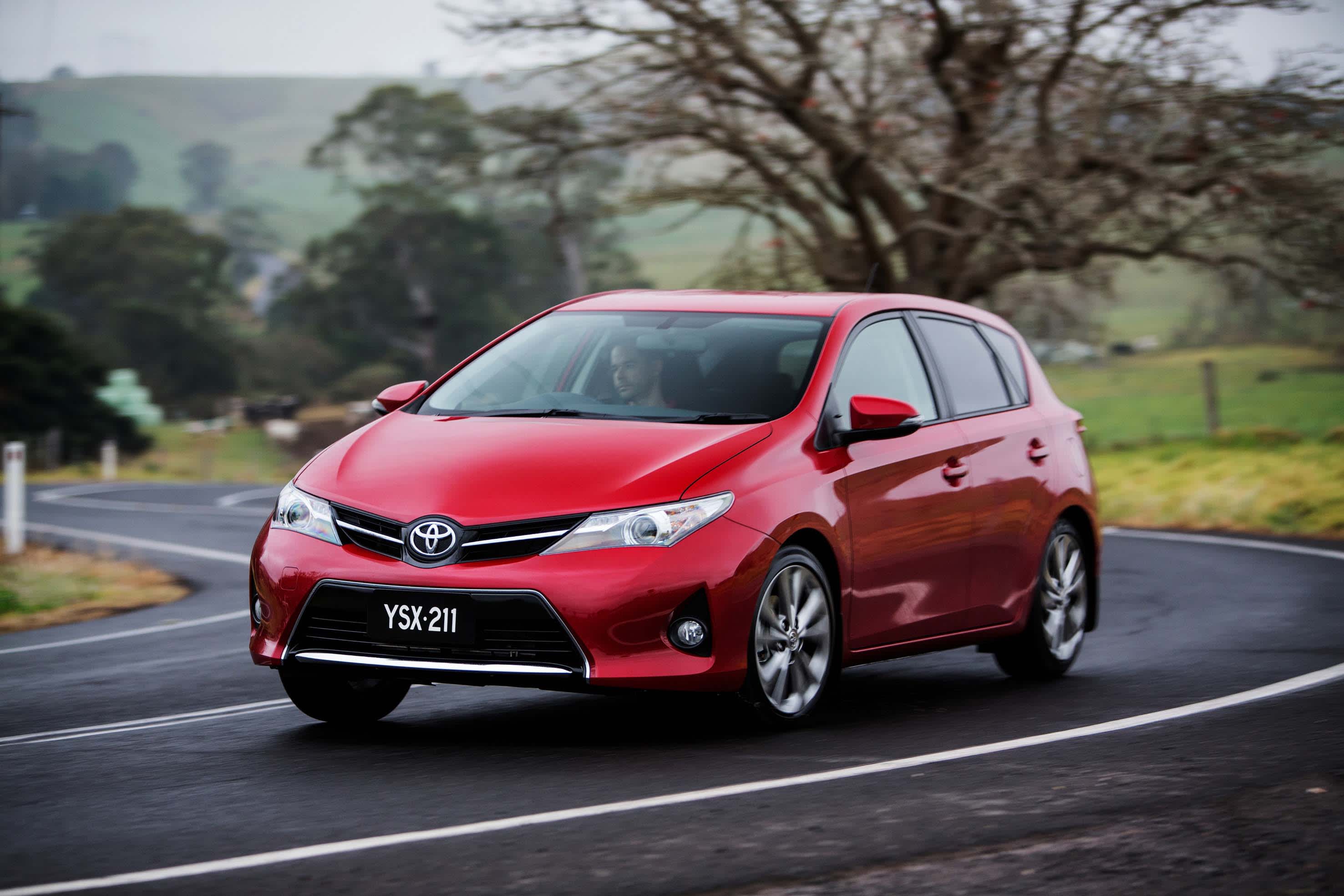 A red Toyota Corolla driving around a bend in a rural road
