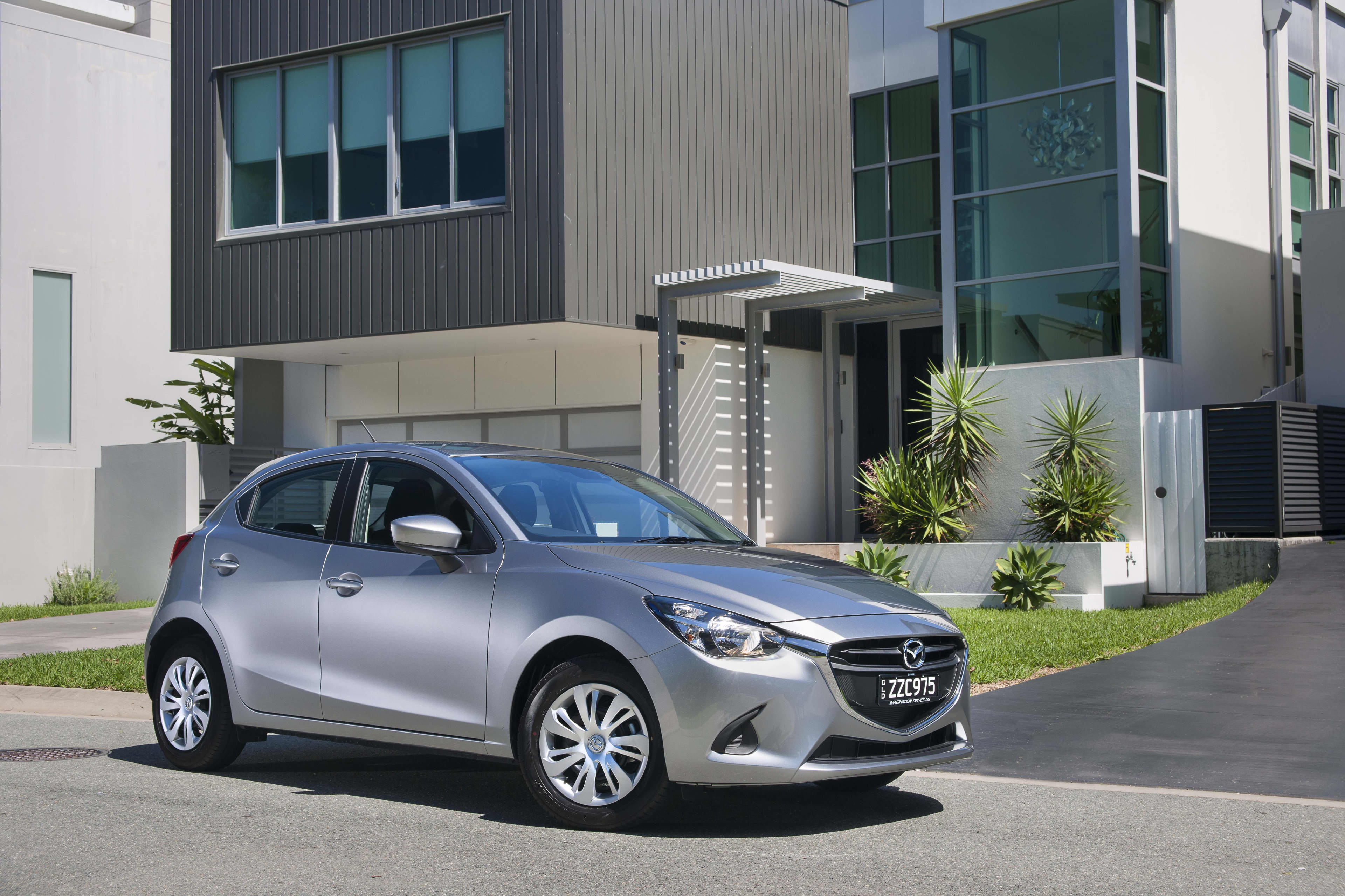 A silver Mazda2 parked outside a modern apartment building