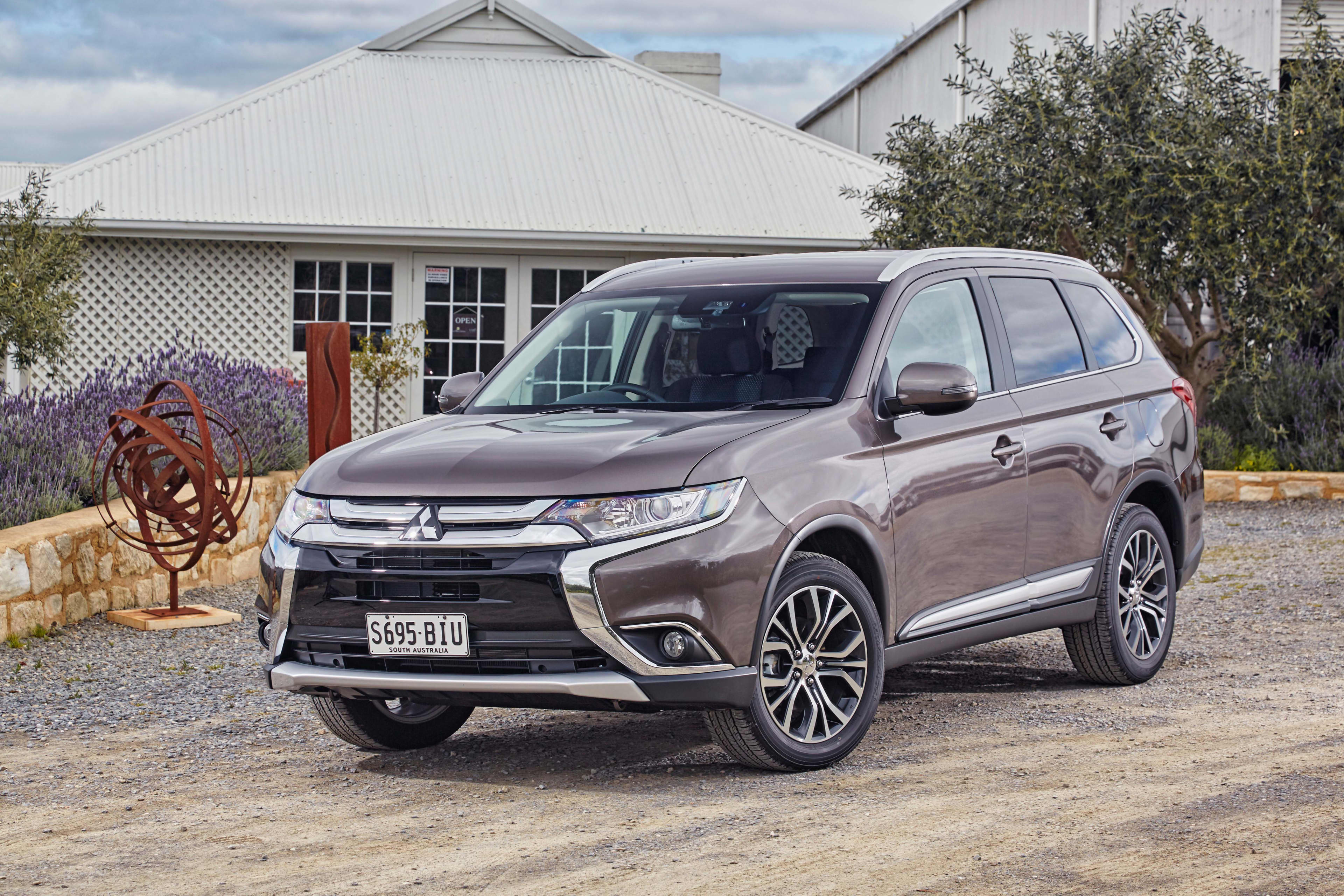 A brown Mitsubishi Outlander parked outside a rural home