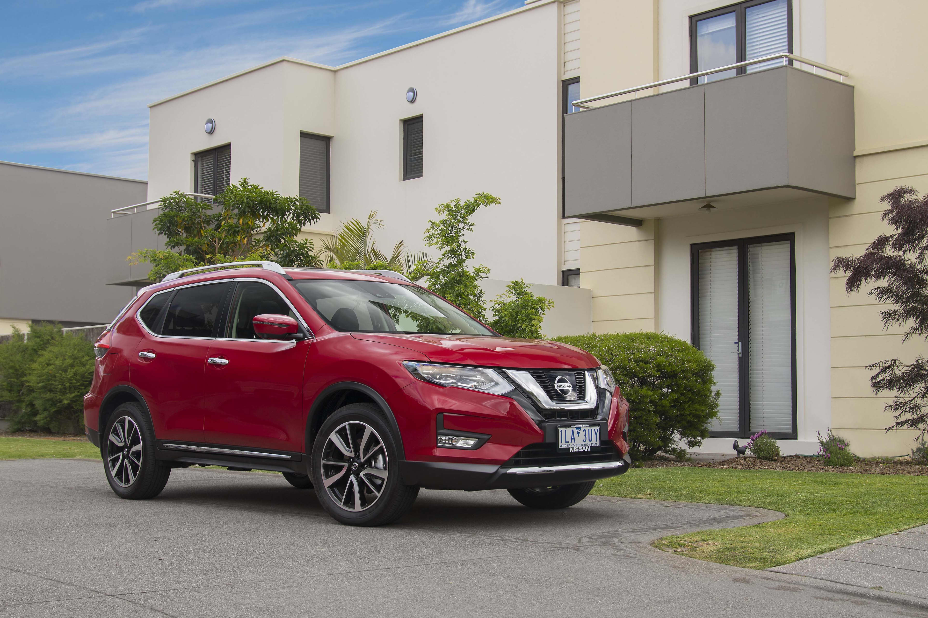 A red Nissan X-Trail parked outside a modern apartment building