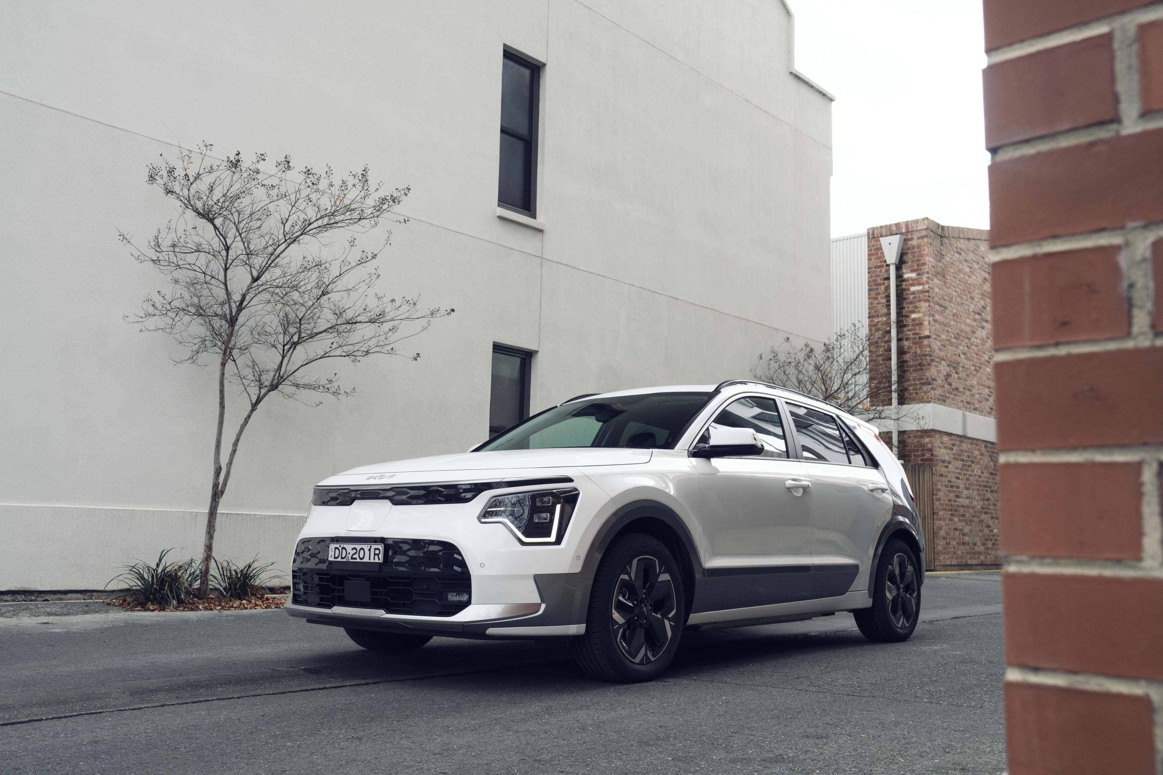 A white Kia Niro EV driving past a building.