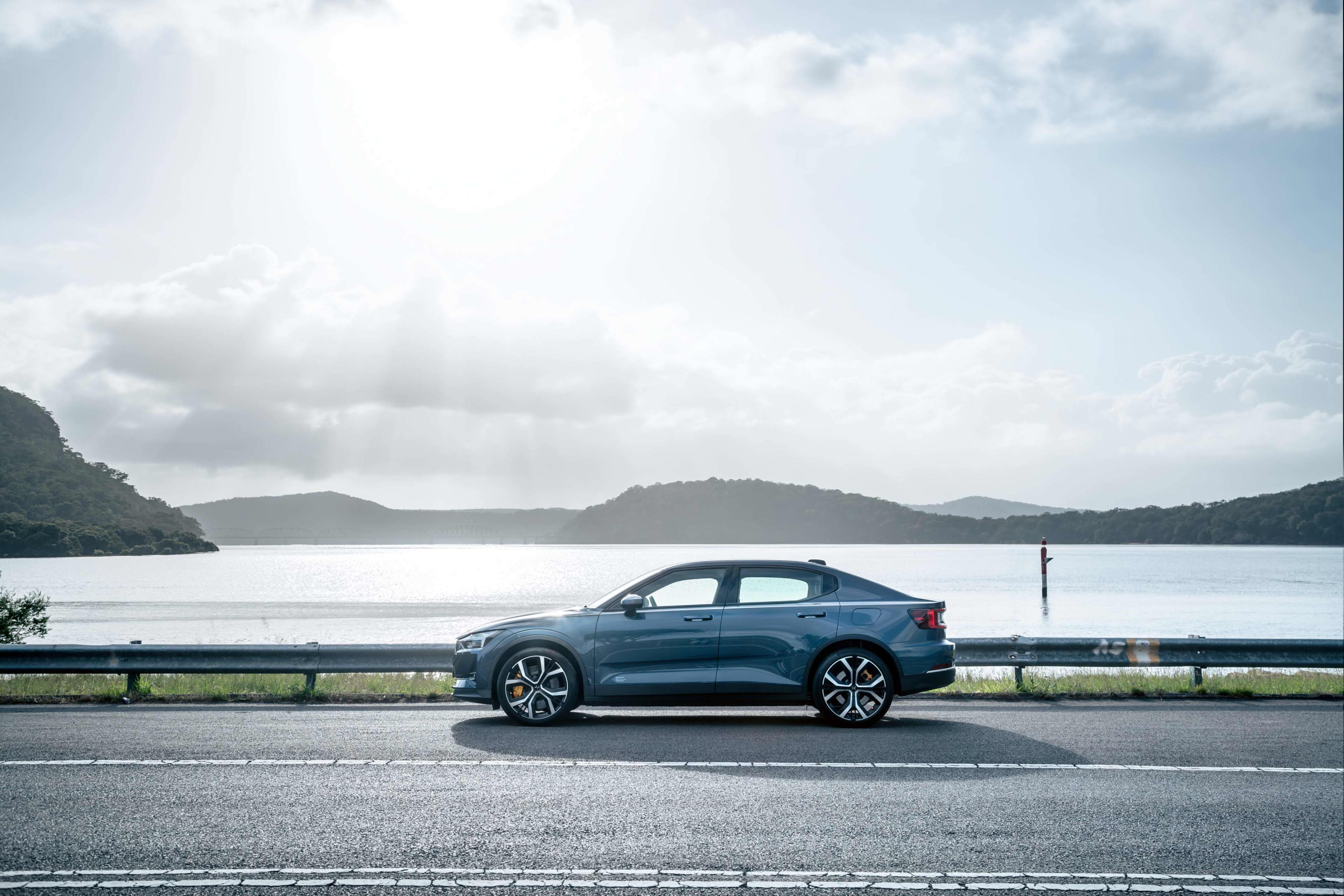 A blue/silver Polestar 2 EV, described as having a CATL battery, parked on the side of a road next to a river.