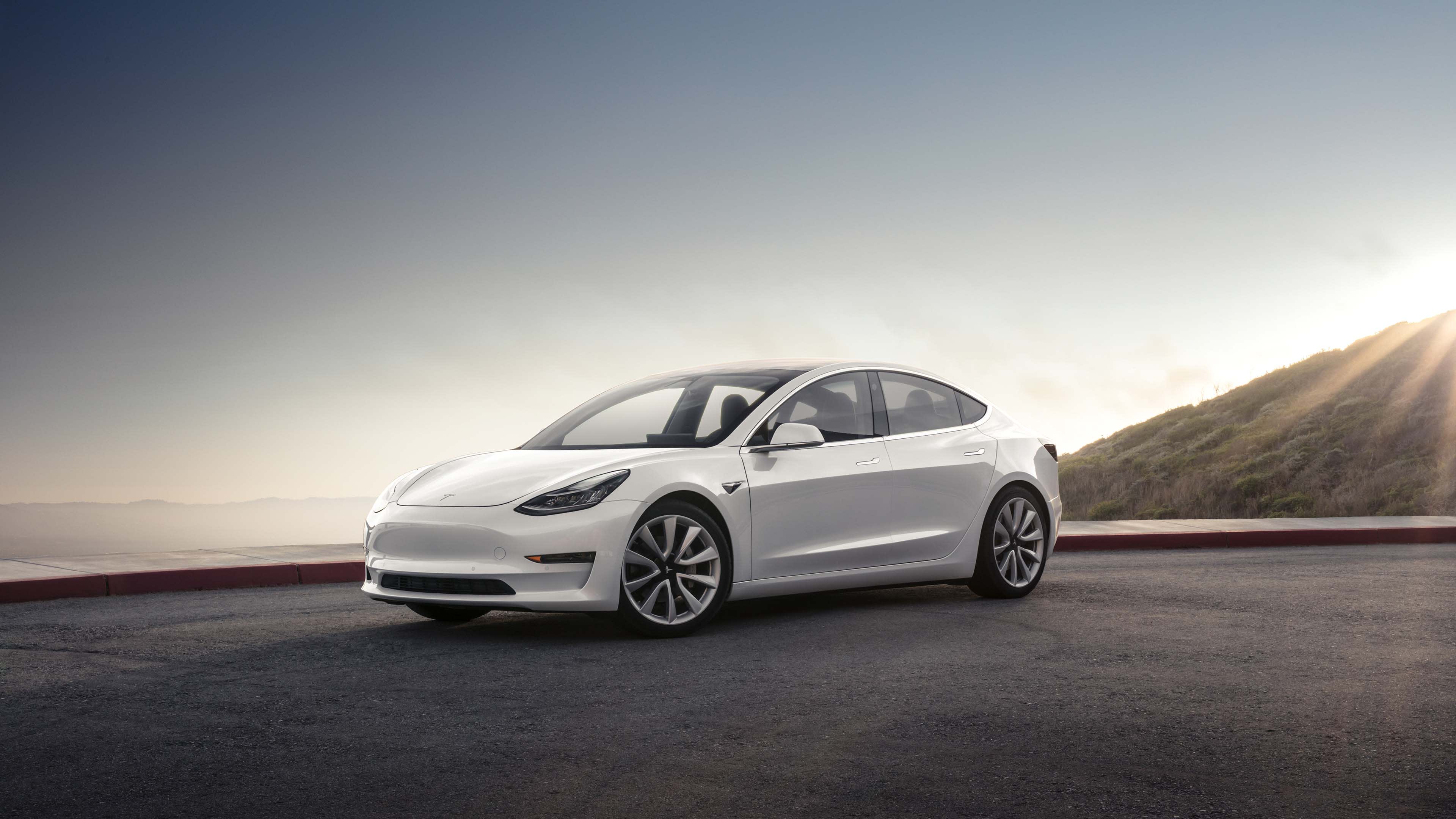 A white Tesla Model 3 EV parked in a beach carpark.