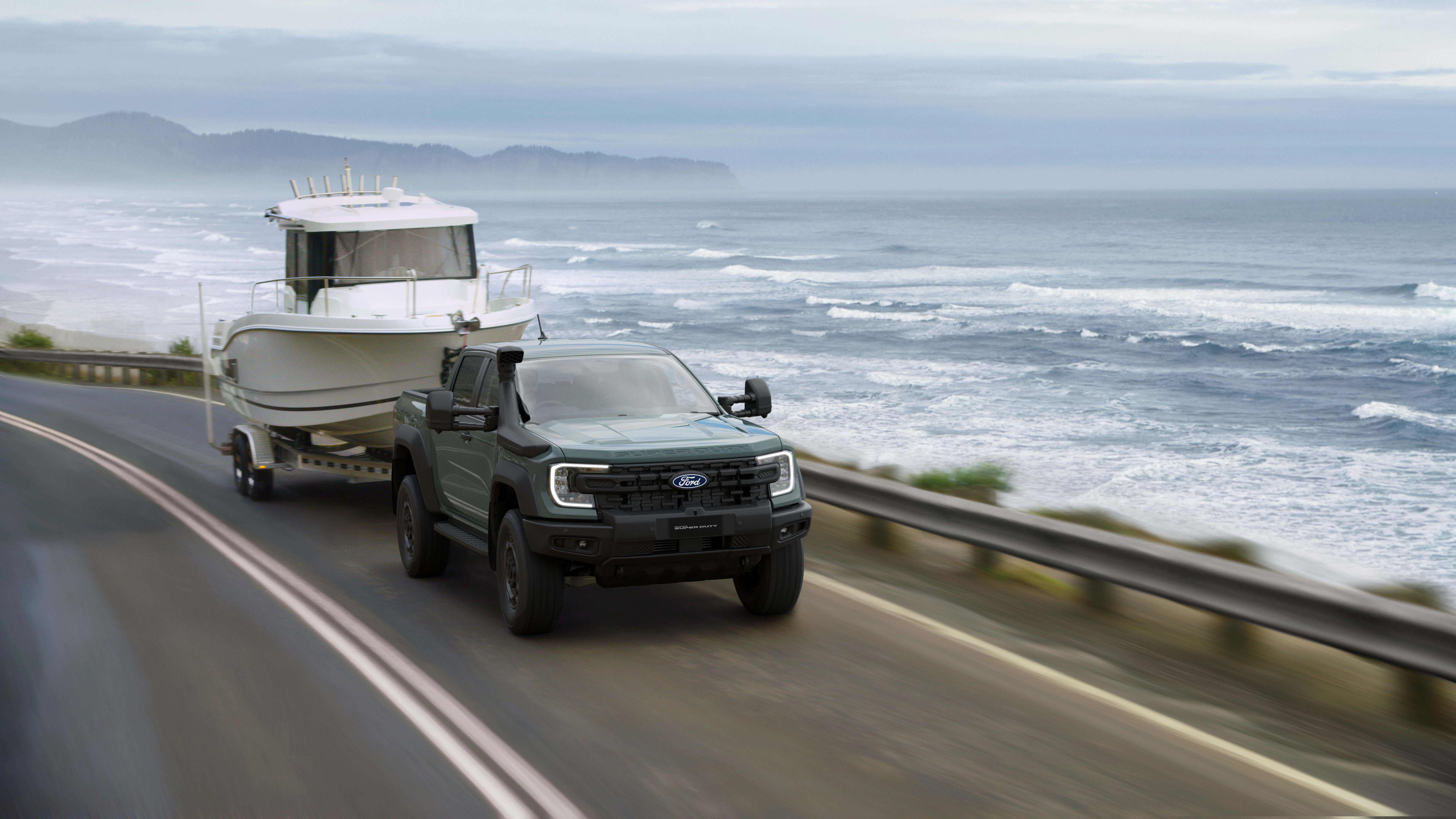 A dark coloured Ford Ranger Super Duty towing a boat along a beachside road.