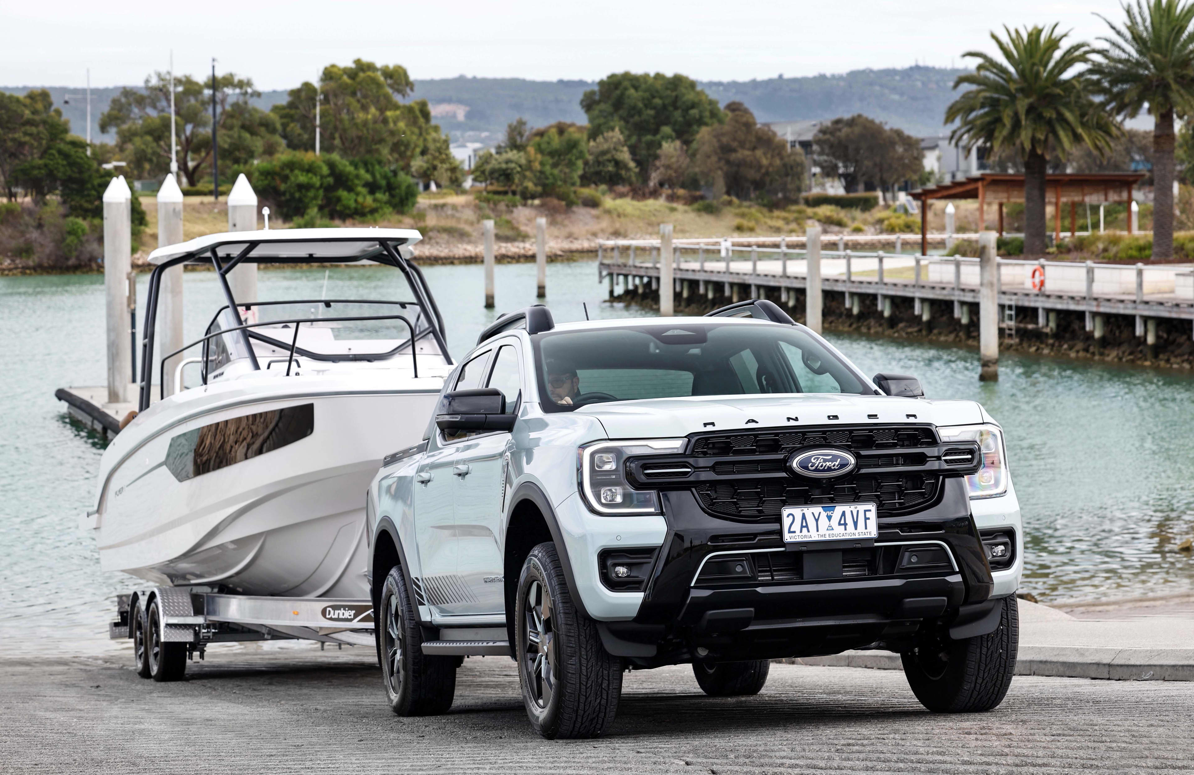 A white Ford Ranger towing a boat near a river boat ramp.