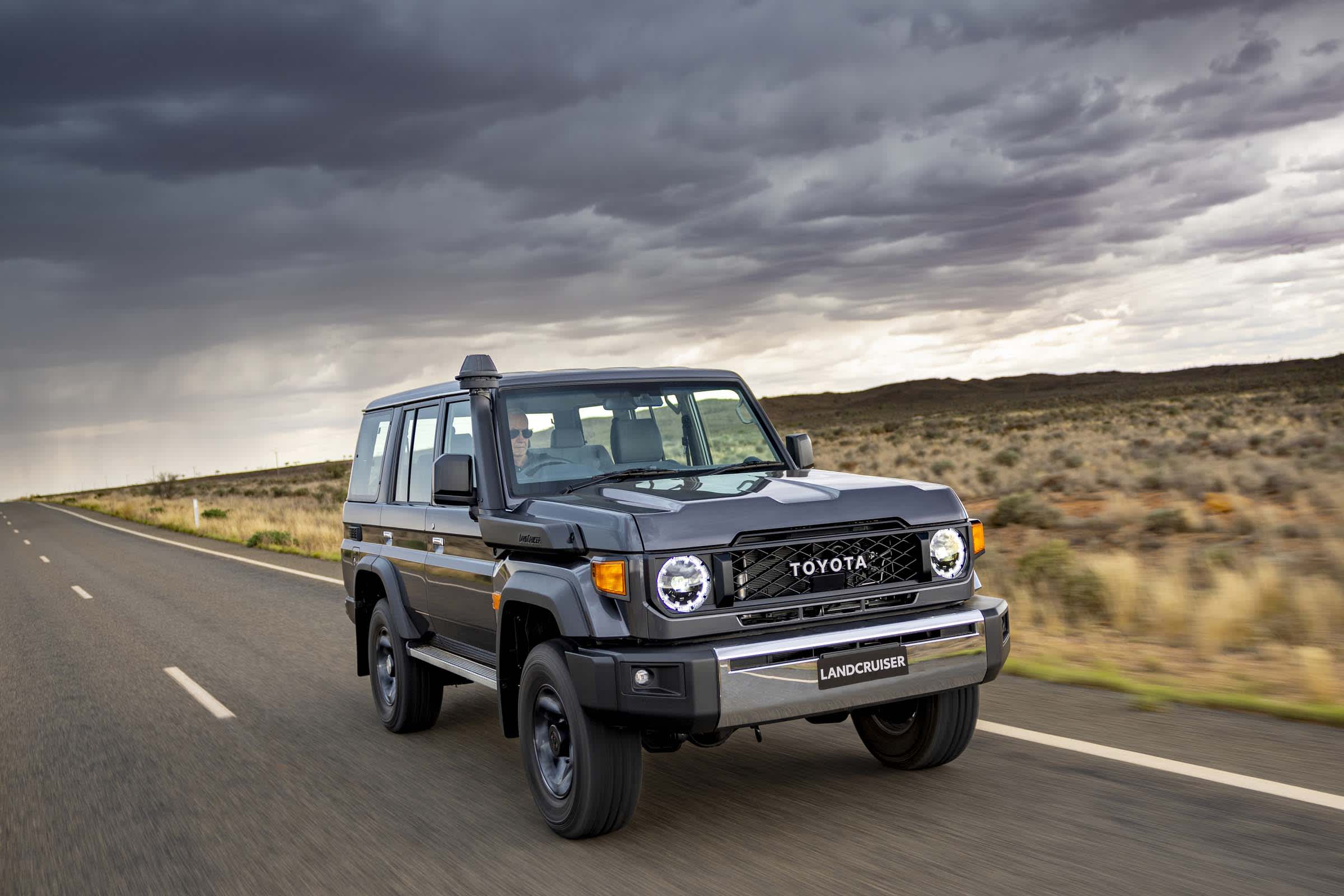 A dark coloured Toyota Landcruiser driving on a country road.