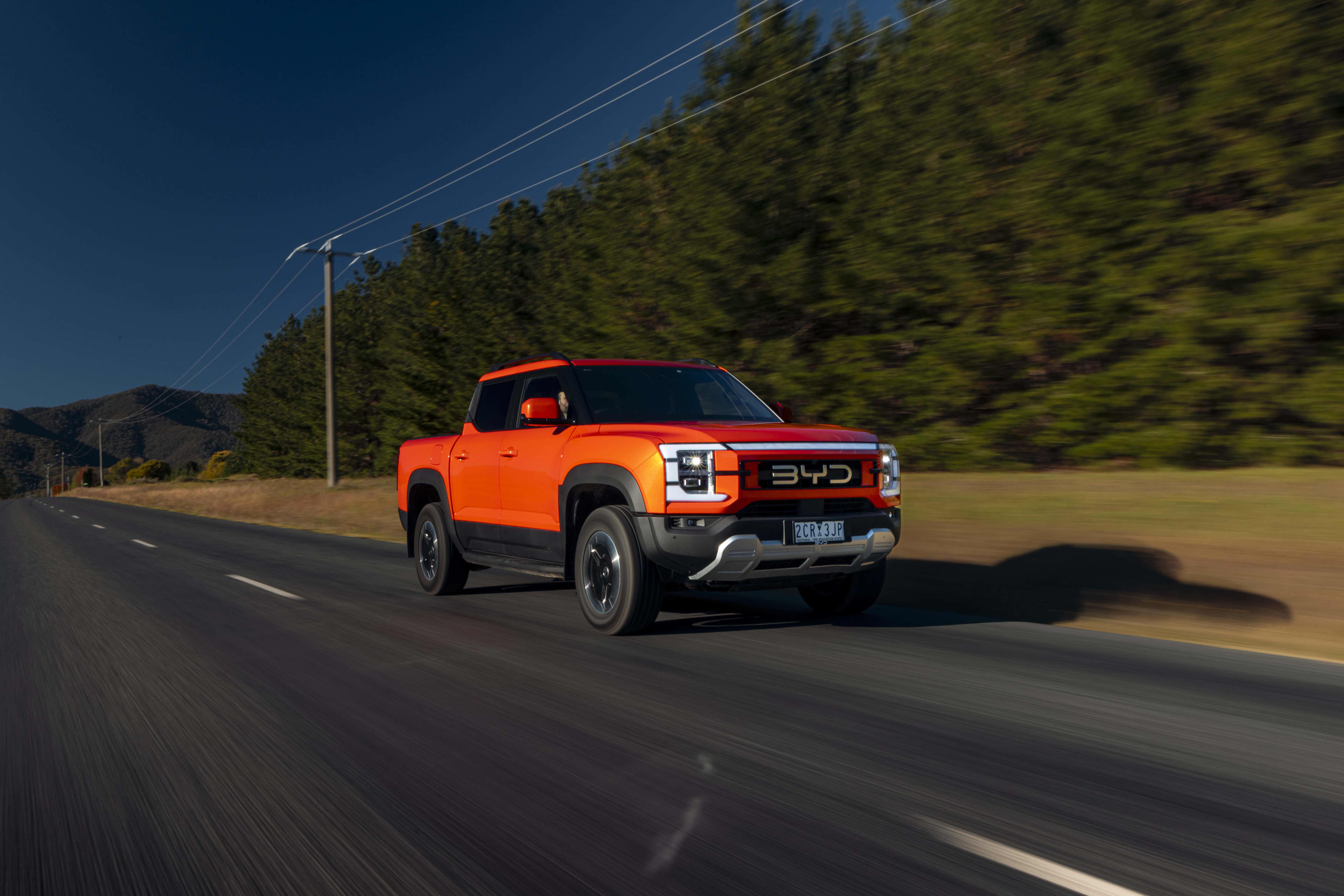 An orange-red BYD shark driving on an open road with trees in the background.