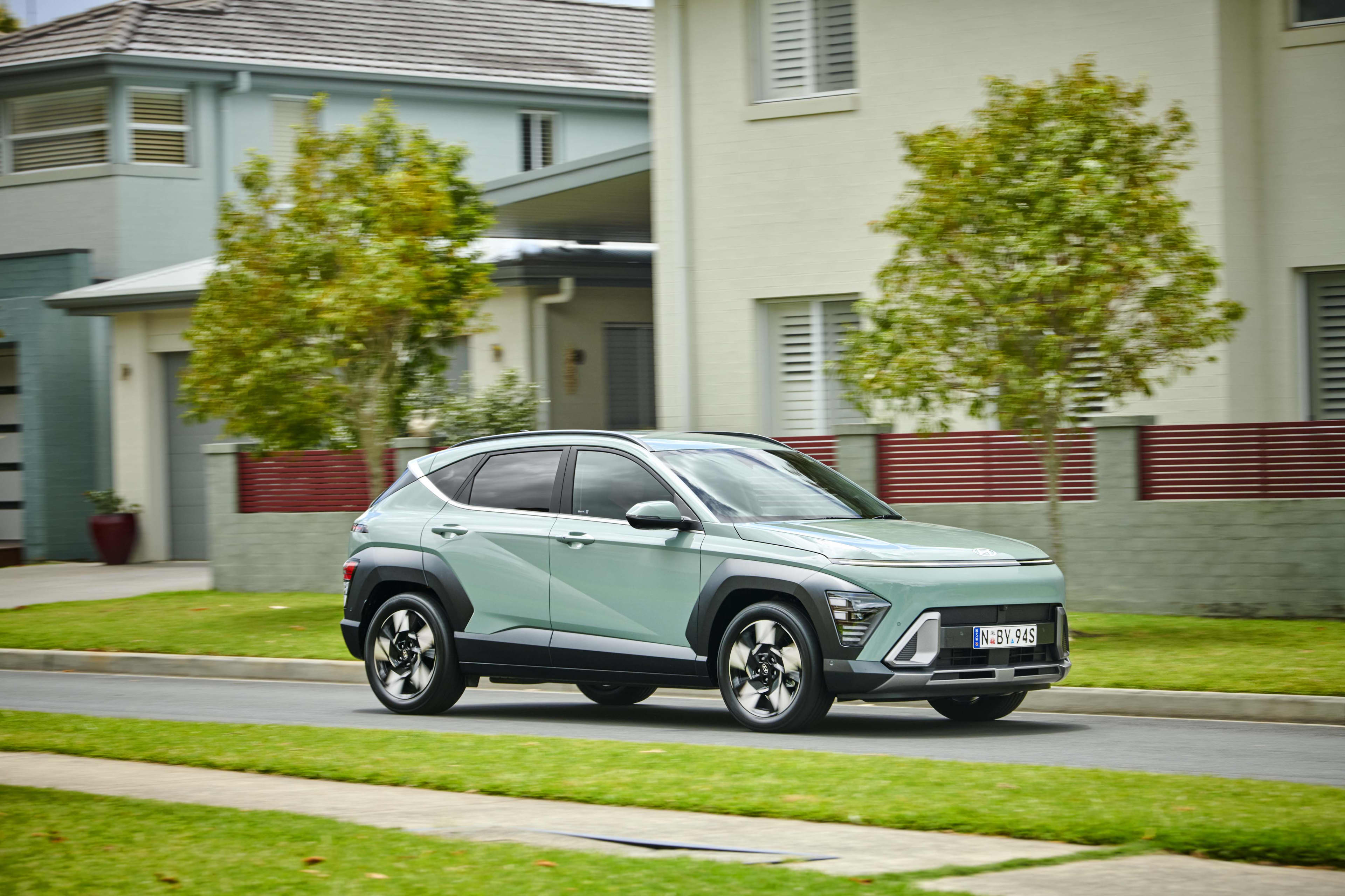 A mint green Hyundai Kona EV driving along a tree lined residential street.