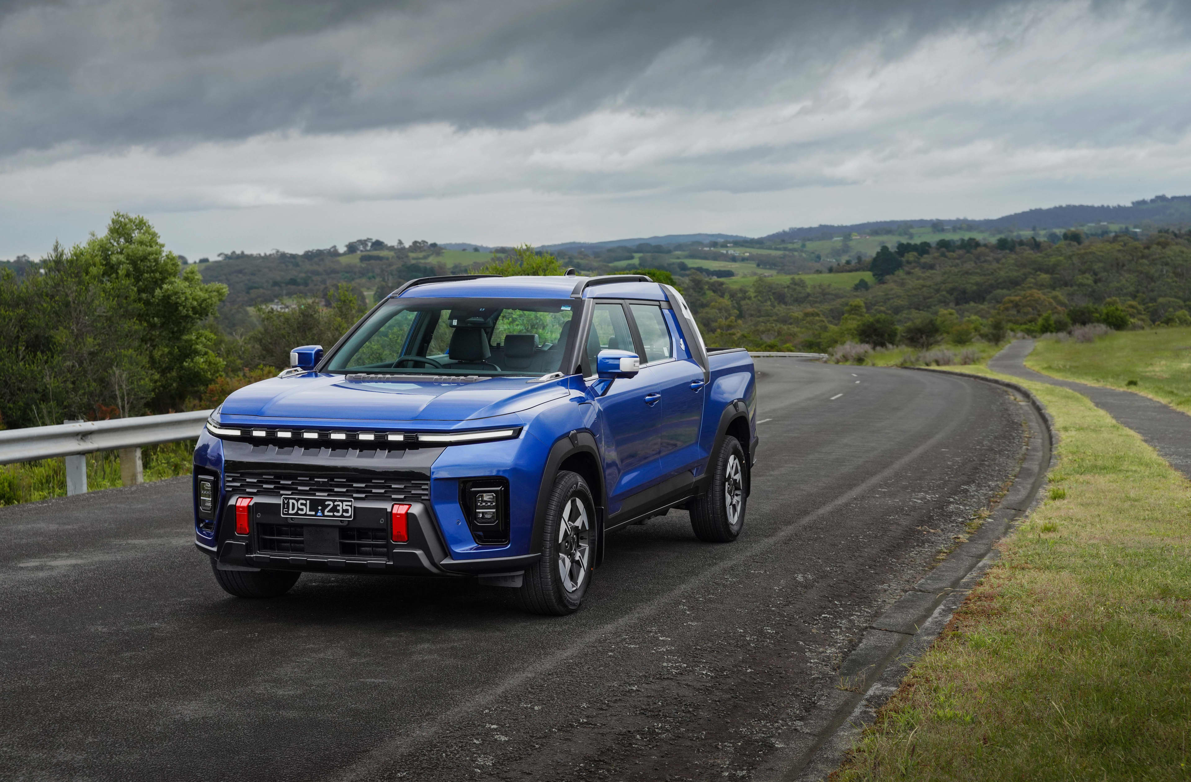A blue KGM Musso EV ute driving on a country road.