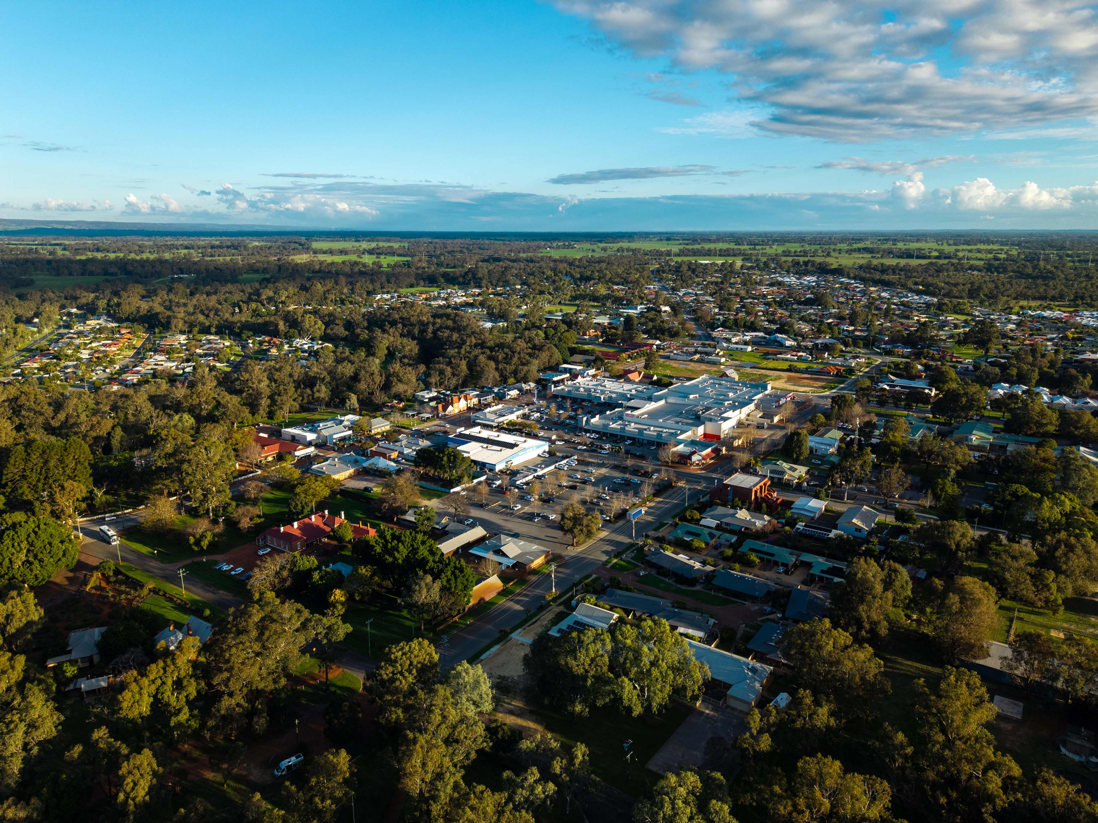 An aerial view of the WA town of Pinjarra, showing buildings nestled in the bushland and a blue sky with white clouds.