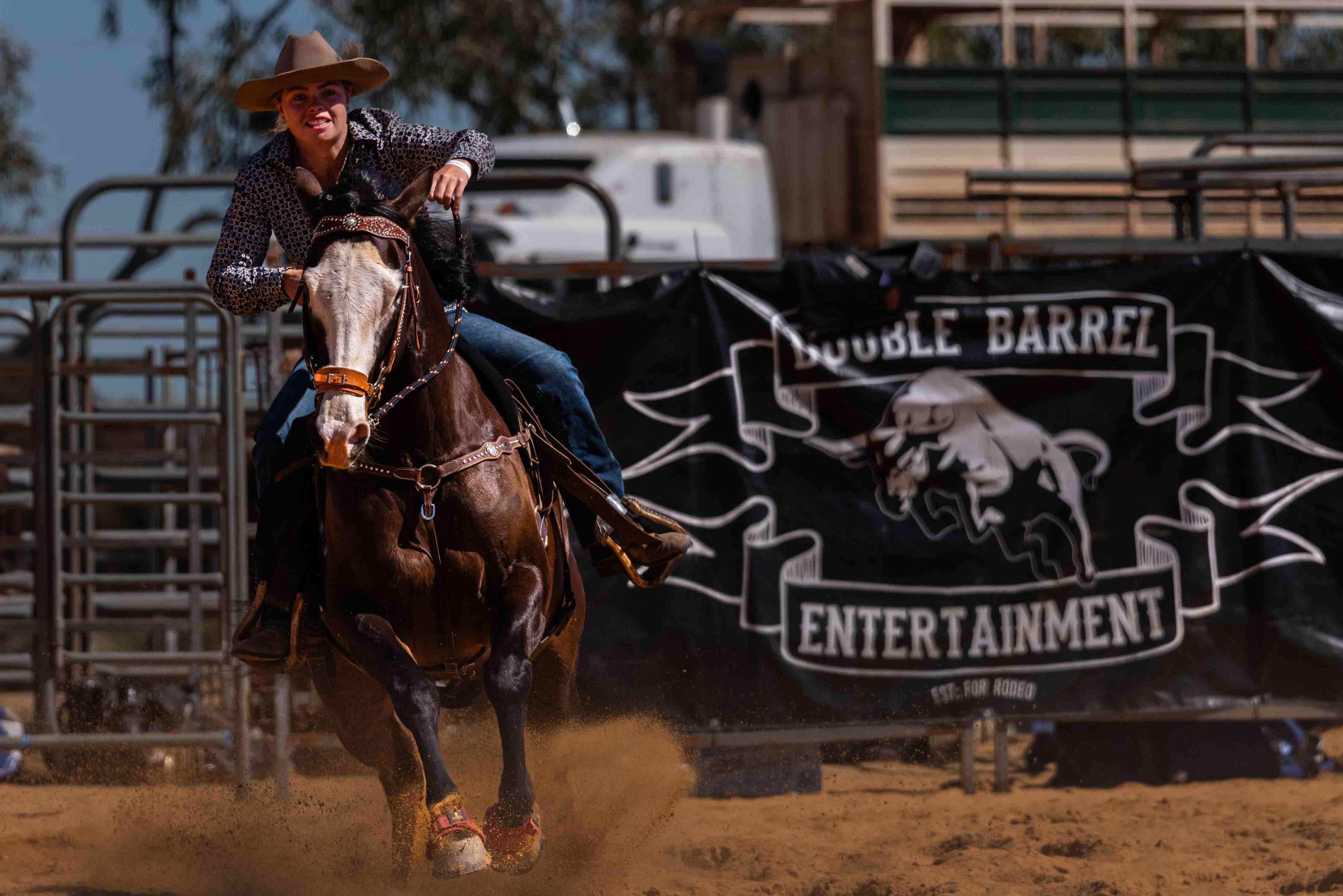 An image of a girl wearing a wide-brimmed hat on a horse racing through red dirt with a sign in the background that reads "Double Barrel Entertainment"