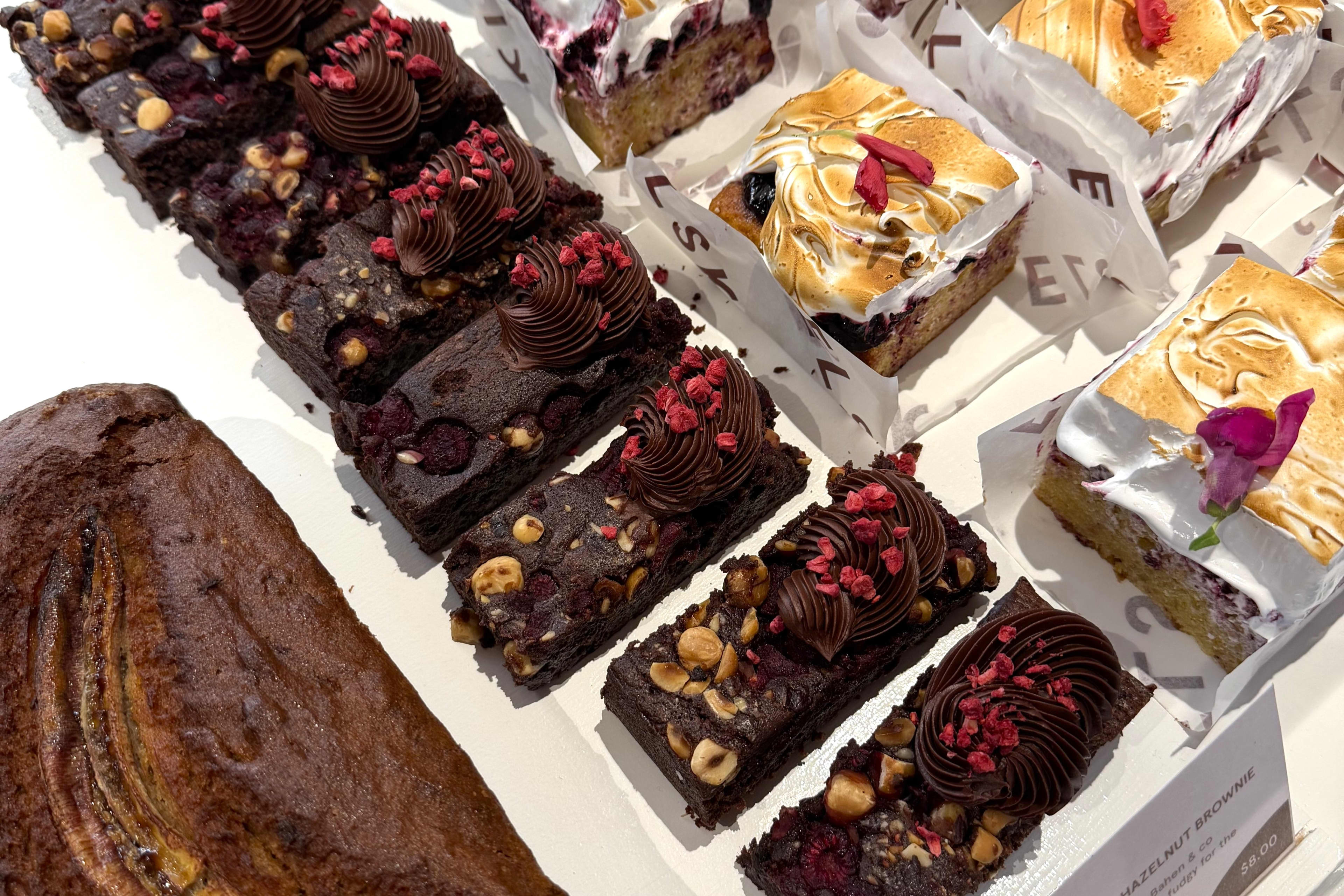A selection of gourmet bakery treats, including rectangular brownies, alongside a square berry cake slice toasted with meringue icing.