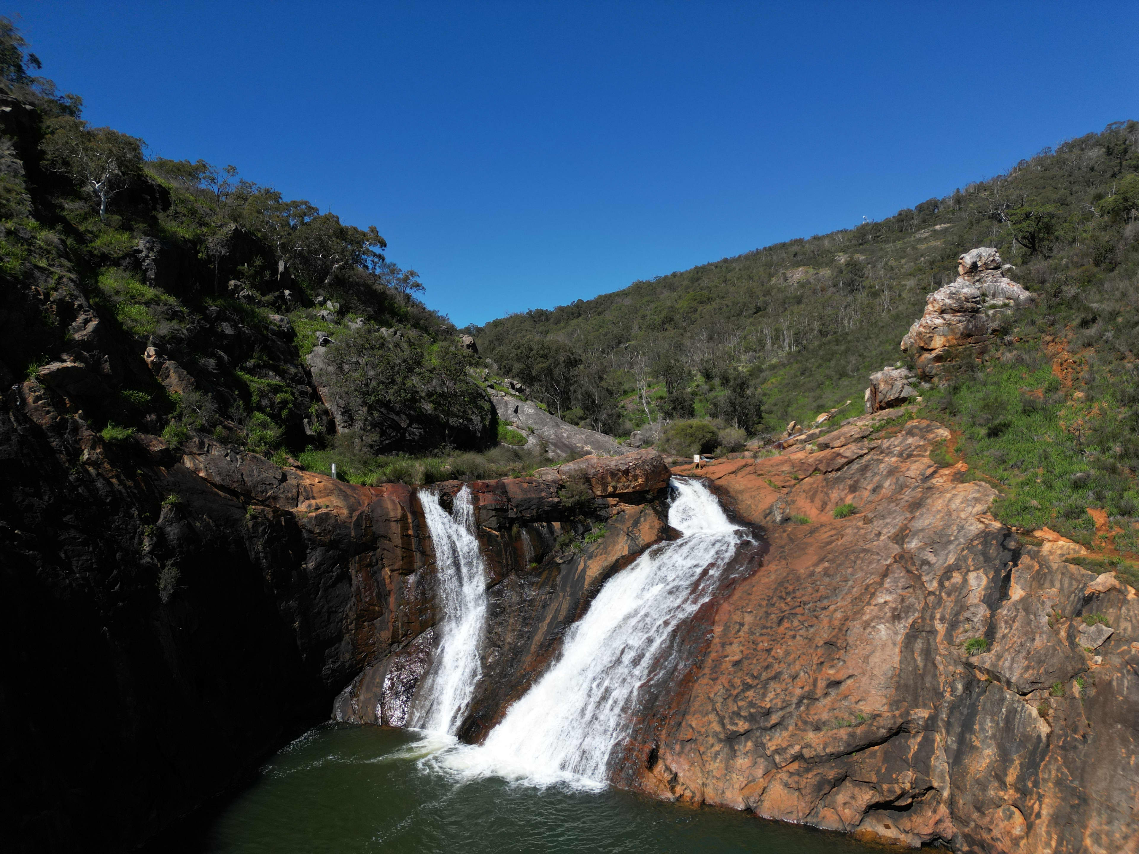A large waterfall cascading over distinct, layered orange and brown rock formations into a body of water.