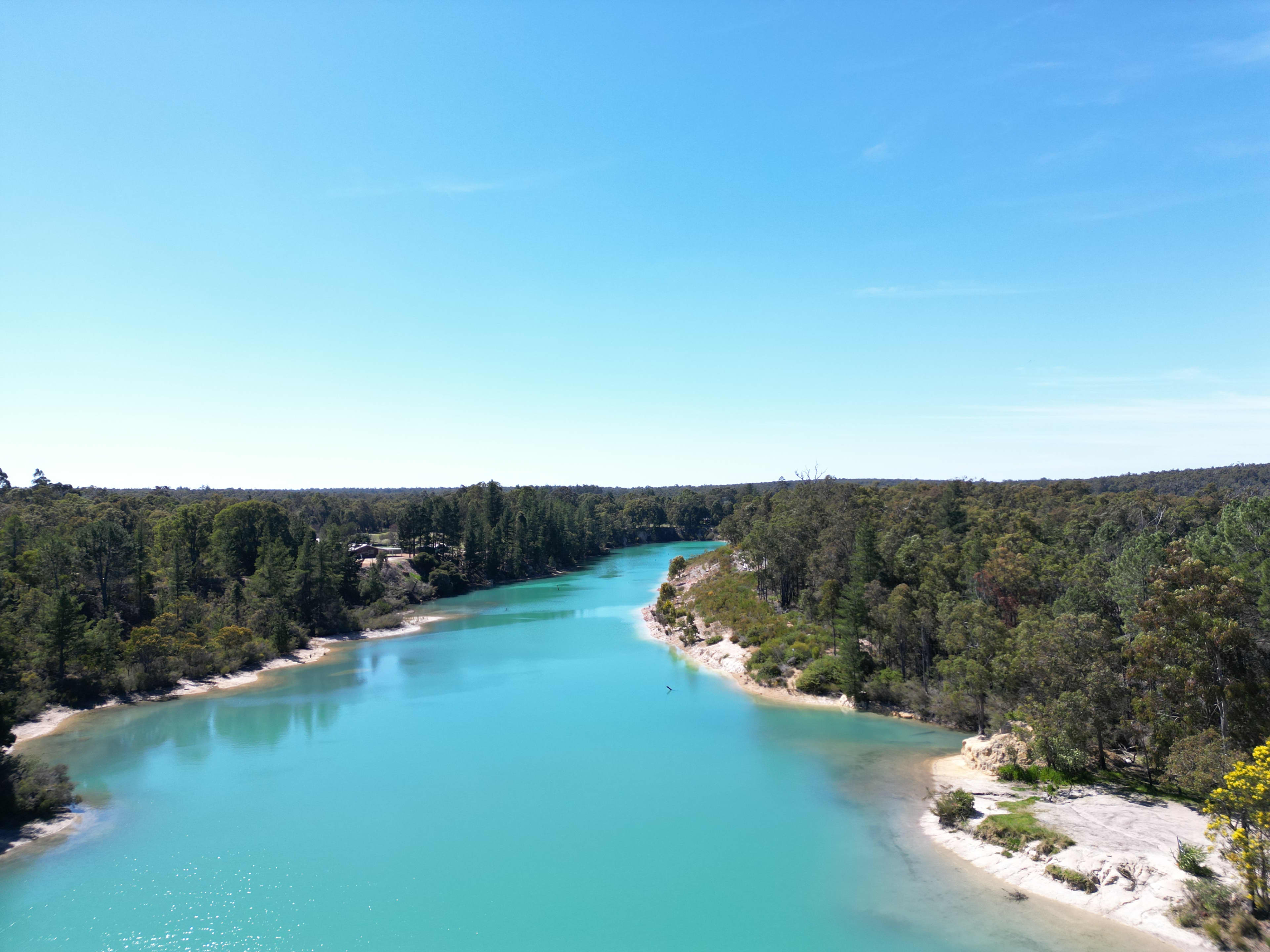 A large body of bright blue water surrounded by sand and green vegetation.