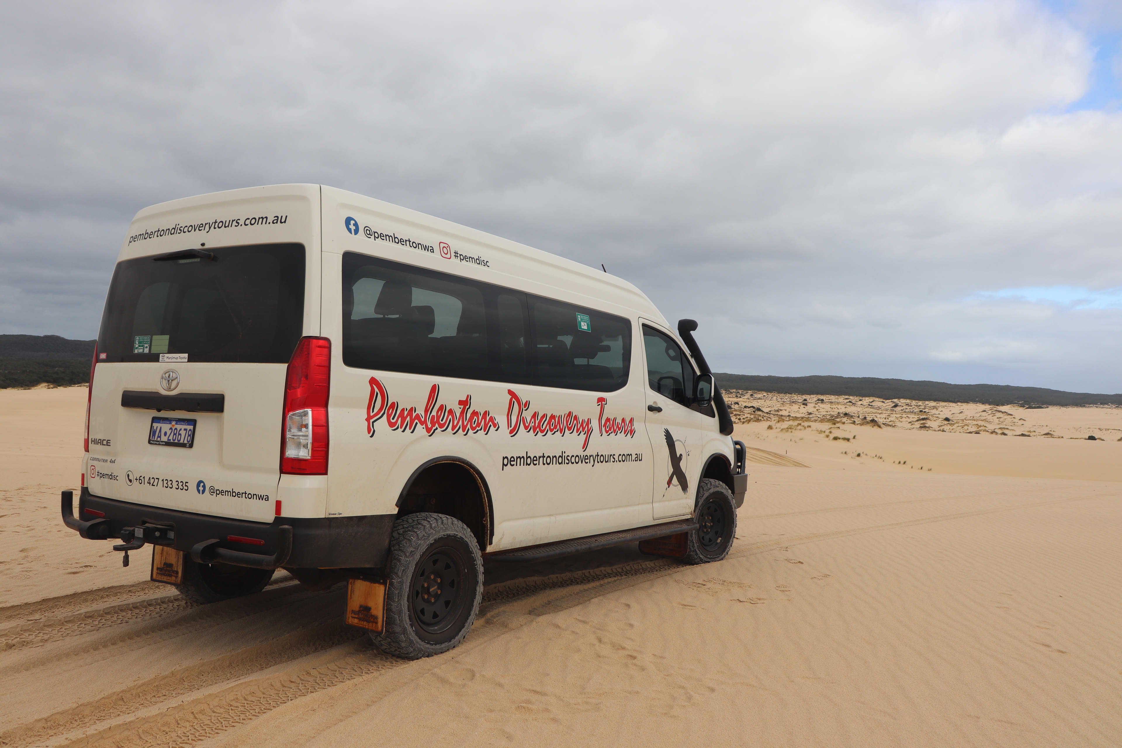 A white off-road van that reads "Pemberton Discovery Tours" parked on creamy sand dunes.