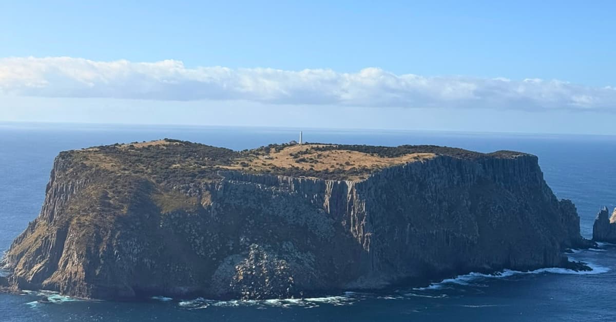 Island surrounded by dark ocean with lighthouse on it
