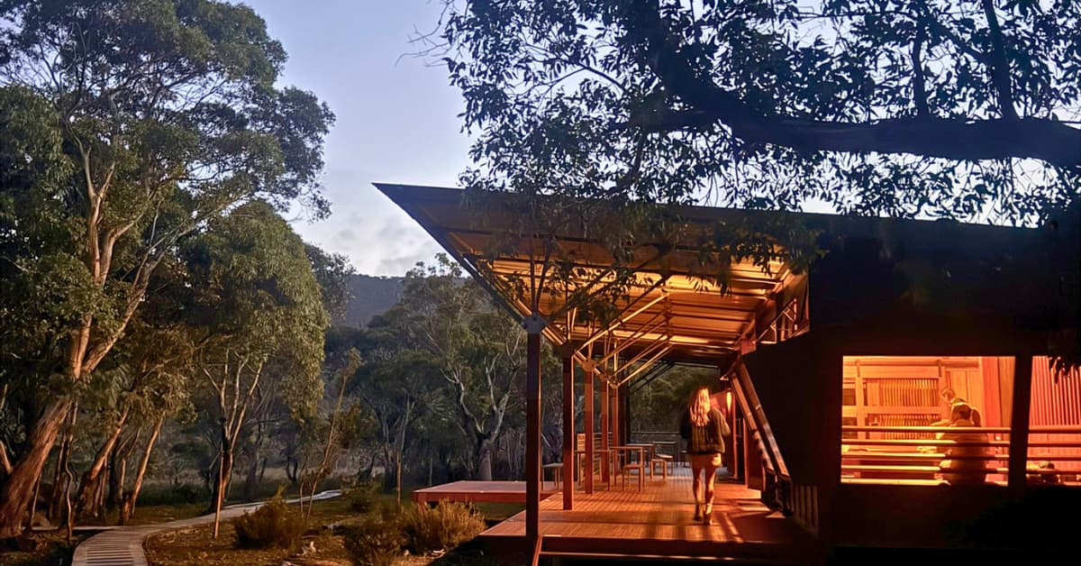 A large wooden cabin in bushland lit up in evening