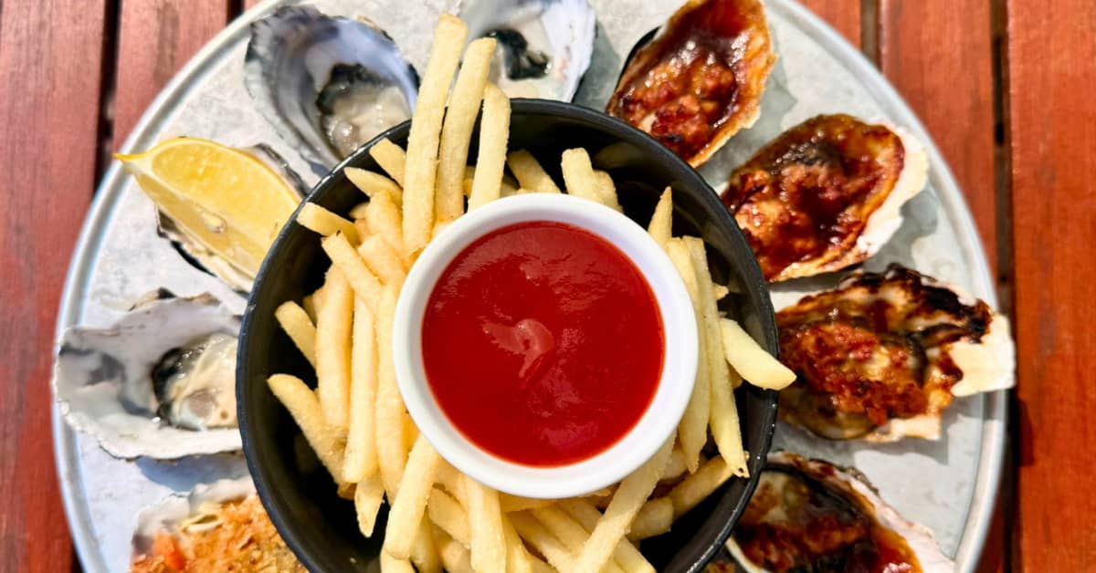 Round plate of different oysters with golden french fries in centre