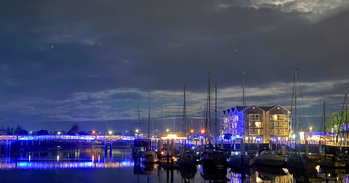 Bridge adorned in lights with boats docked at wharf in evening