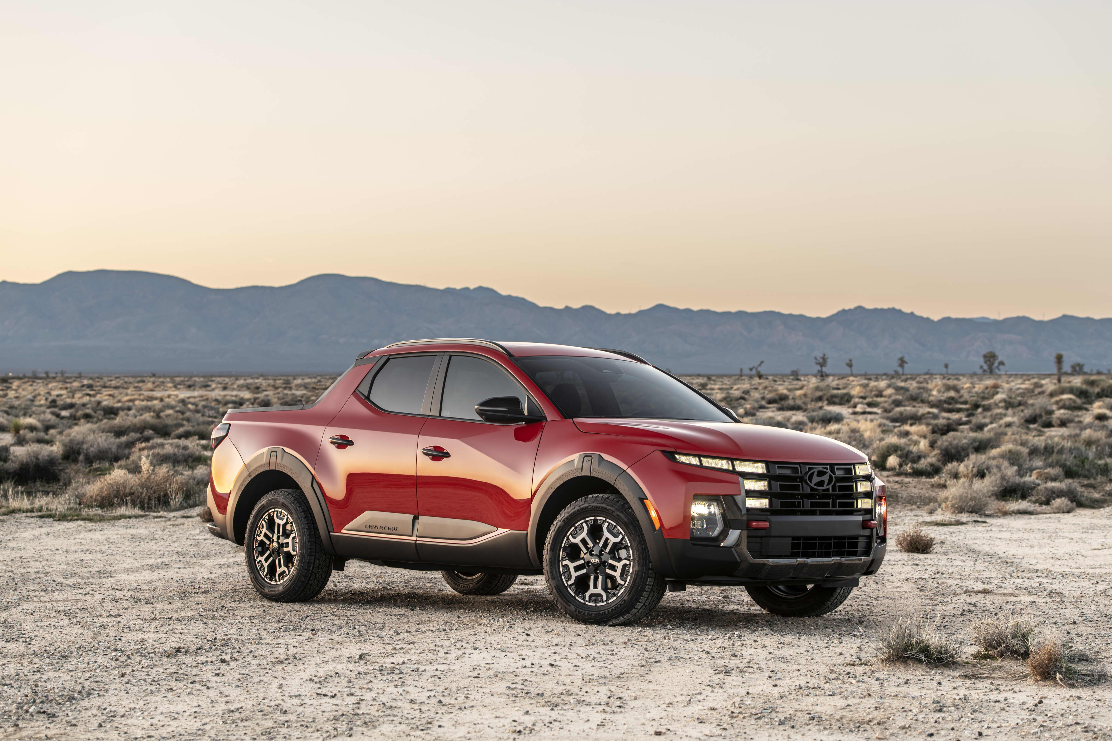 A red Hyundai Santa Cruz XRT ute in North America, in a desert landscape with low shrubs and a ridge in the distance.