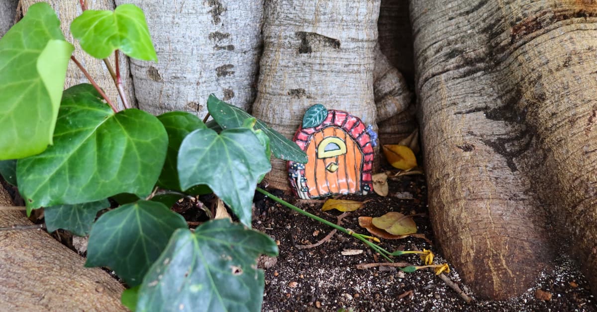 Tiny fairy door near trunk of tree surrounded by lush green plants