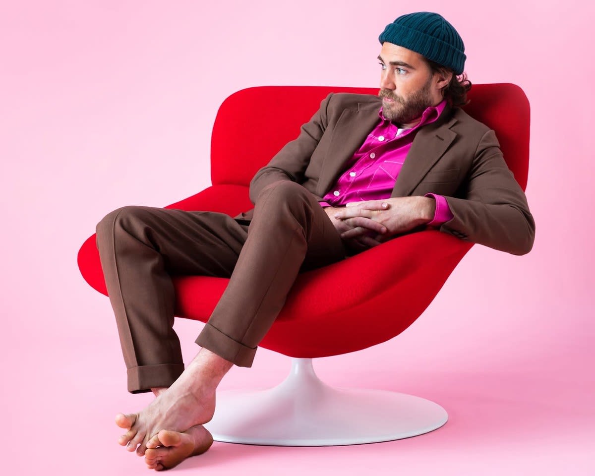Man sitting in chair wearing beanie with no shoes on.