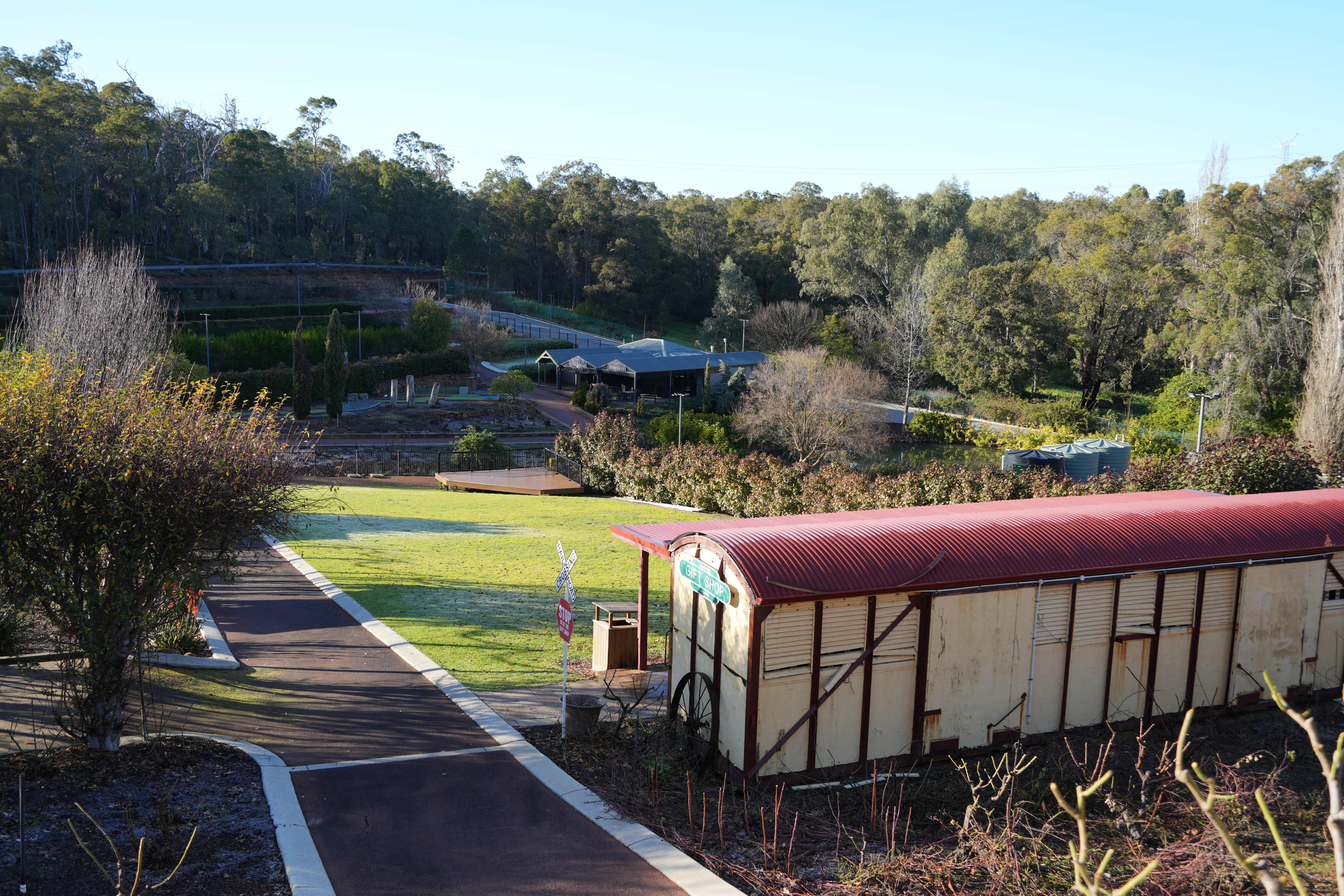 An outdoor park scene featuring a small-cream coloured rustic shed with a curved, reddish-corrugated metal roof in the foreground.