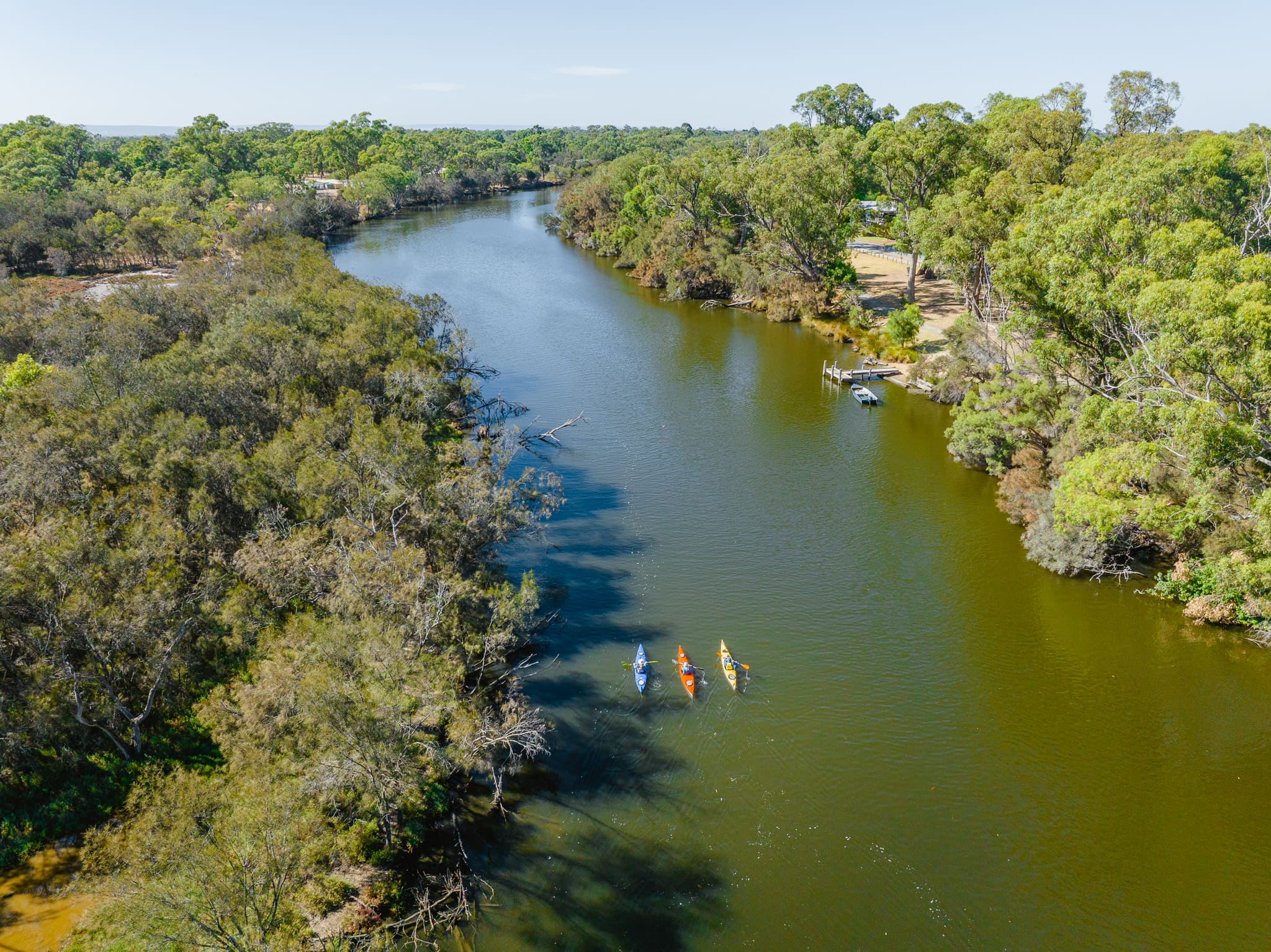 An aerial shot of three kayakers in a river surrounded by bushland.